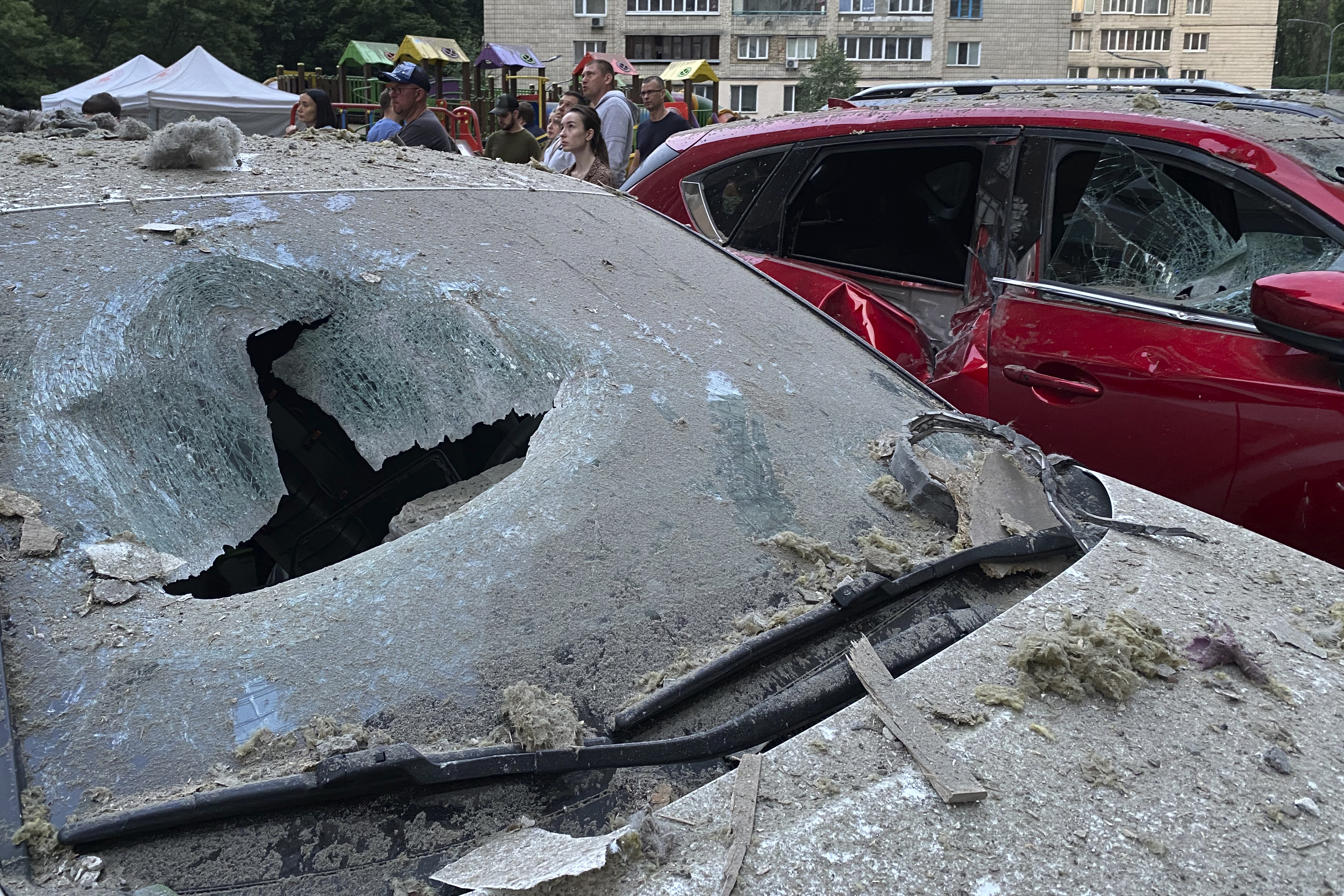 People stand at a parking with damaged cars in front of a multi-story apartment building after Russian attack in Kyiv. Photo / AP