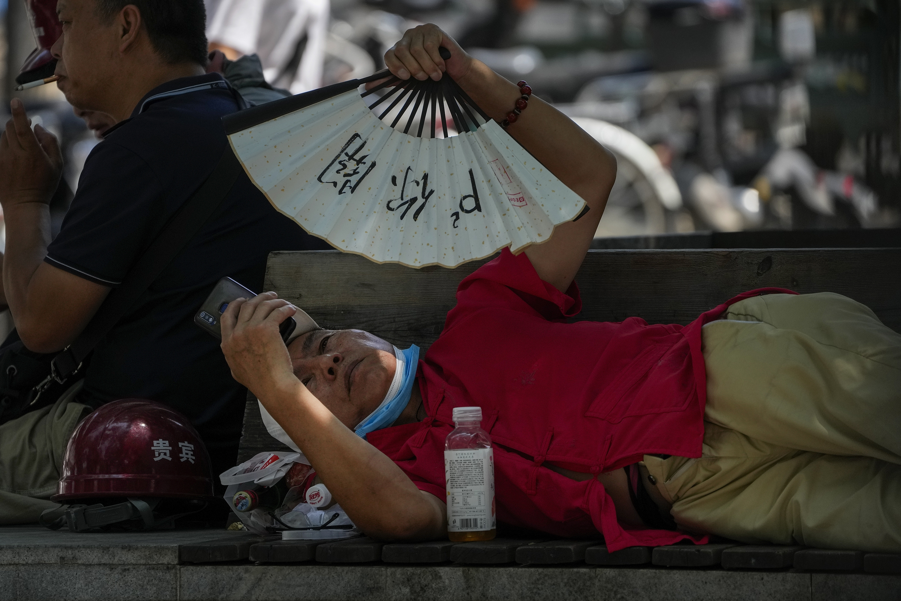 A man cools himself with a fan while browsing his phone on a sweltering day in Beijing. Photo / AP