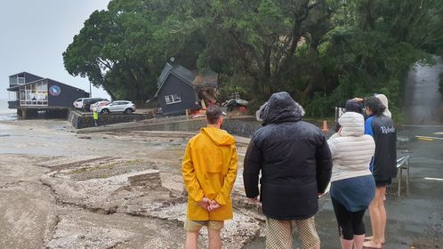 Residents at French Bay in west Auckland watch on after a slip damaged the Coastguard building. Photo / Meg Liptrot