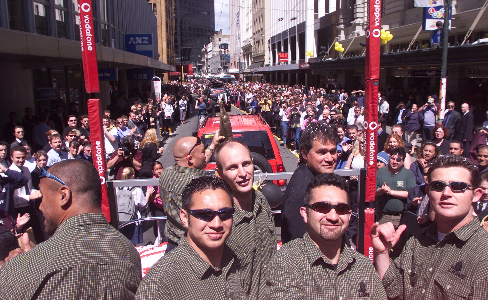 Wellington fans line Lambton Quay for Lions players from left, Jonah Lomu, Norm Hewitt, Shannon Paku, Jason O'Halloran, coach Dave Rennie, Brad Fleming and David Holwell during their parade through the city to celebrate their victory in their NPC title in 2000. Photo / Mark Mitchell
