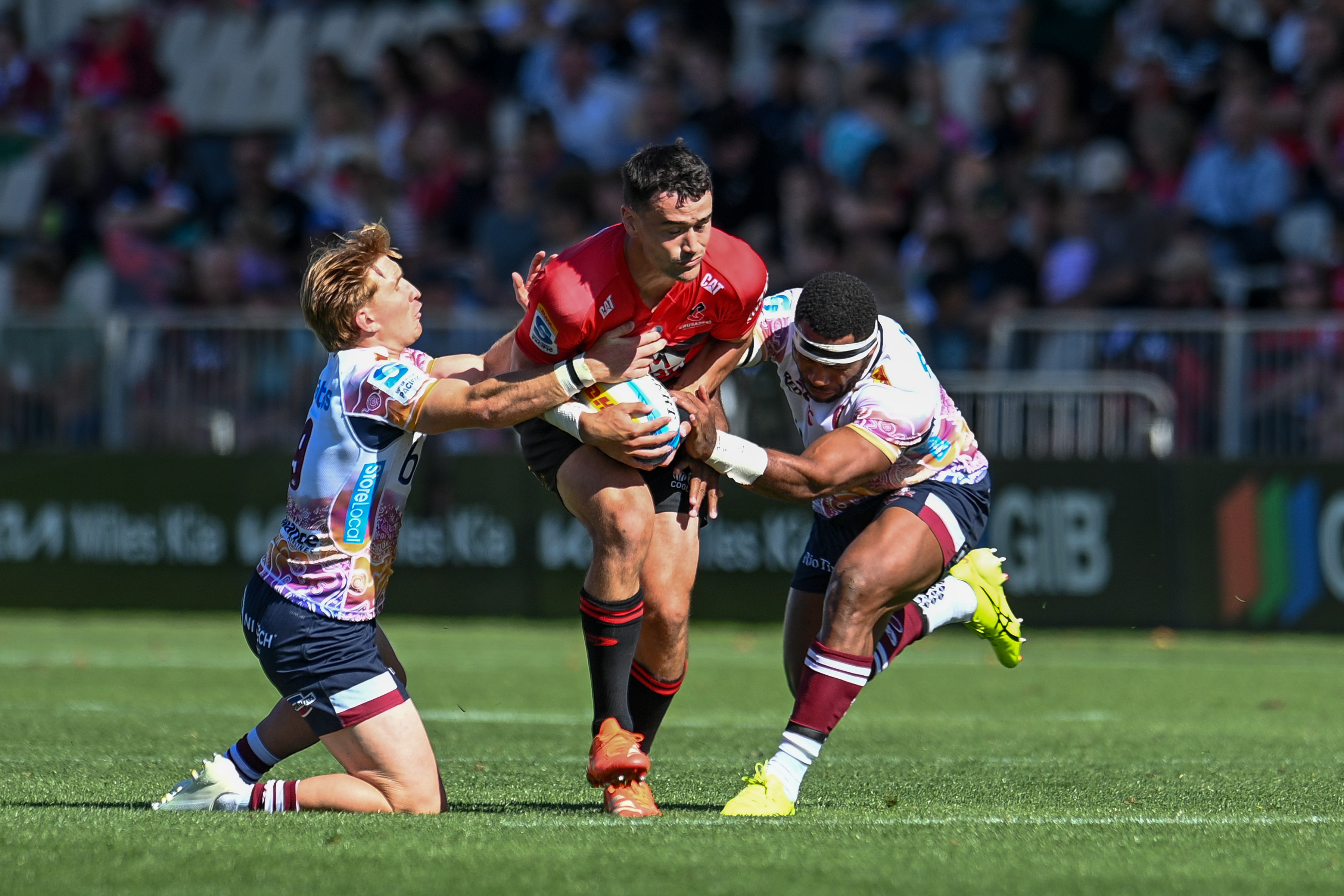 Will Jordan bursting through the tackles of Tate McDermott and Filipo Daugunu during the Crusaders vs Reds match at Apollo Projects Stadium in Christchurch on March 9. Photo / Photosport