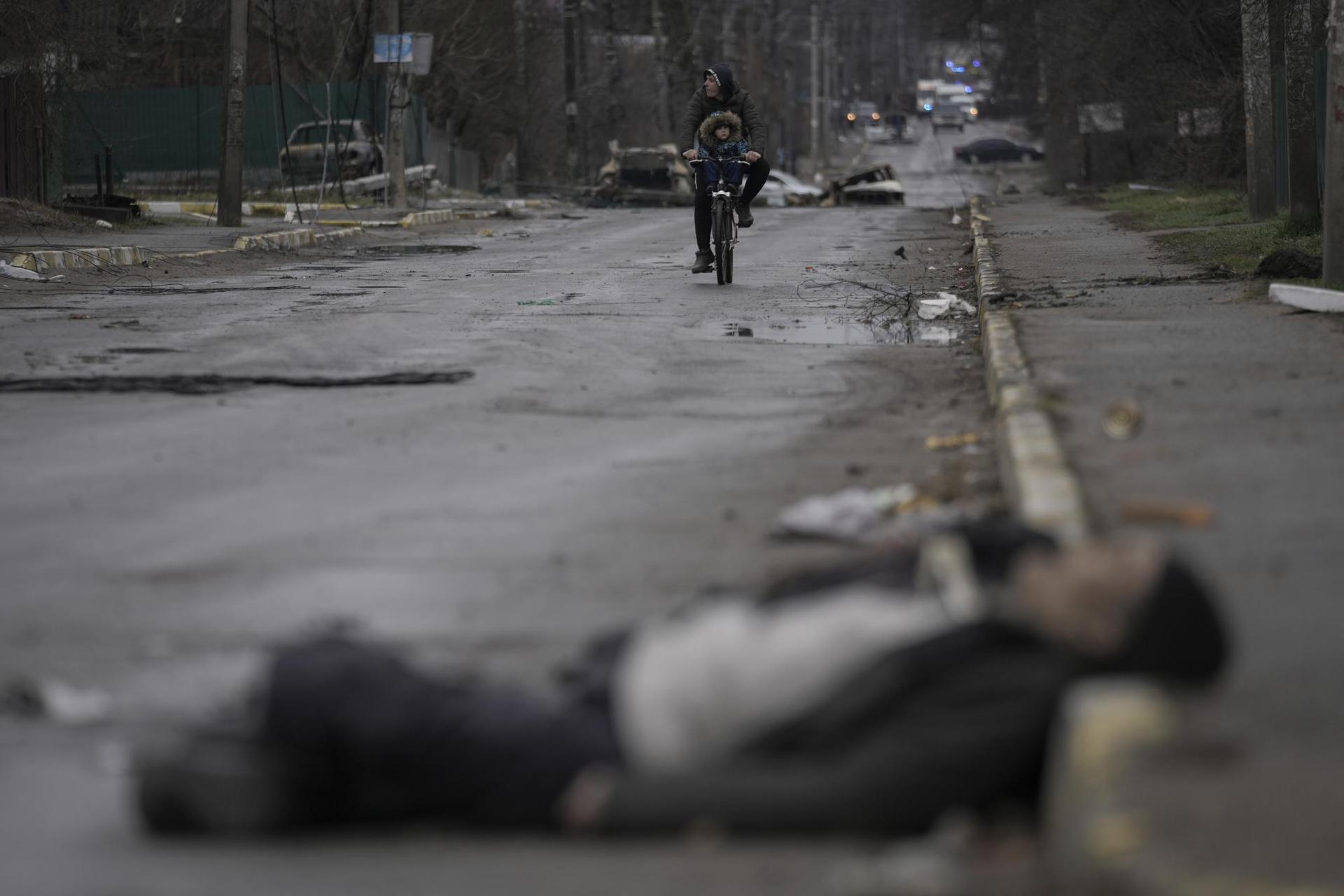 A man and child ride on a bicycle as bodies of civilians lie in the street in the formerly Russian-occupied Kyiv suburb of Bucha, Ukraine, Saturday, April 2, 2022. Photo / AP