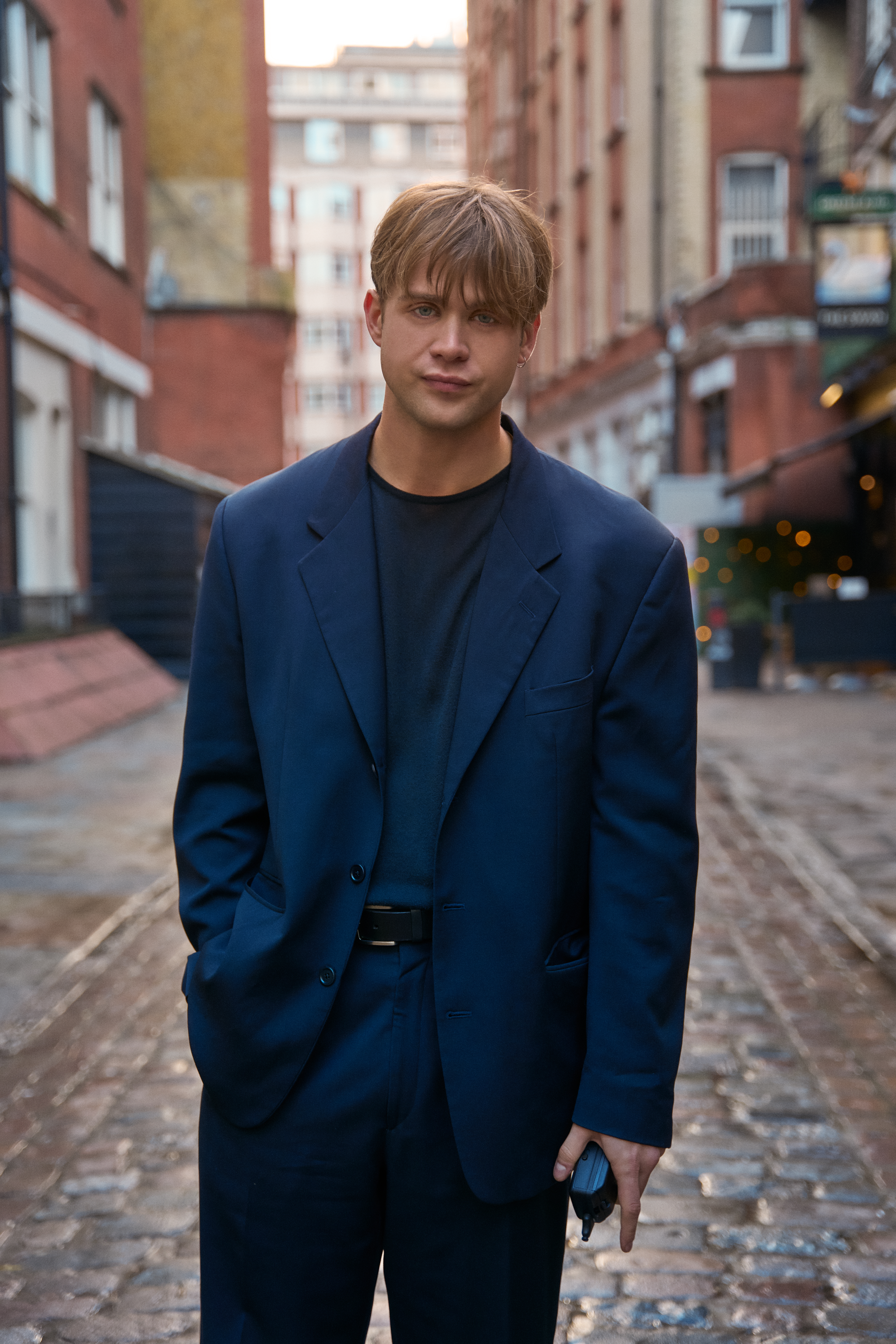 Dex’s wardrobe, featuring oversized blazers, roomy trousers, and cinched waists, reflects the excess of the 90s.