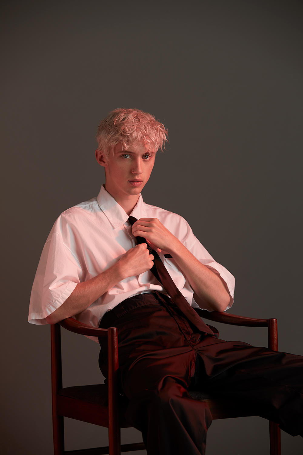 Troye Sivan is proud to be in the LGBTQ music community, but says his sexuality is also besides the point in his music. Prada shirt $845, tie $300 and trousers $1275. McIntosh Rosewood Dining Chair, $4530 (set of eight), from Mr. Bigglesworthy. Photo / Mara Sommer