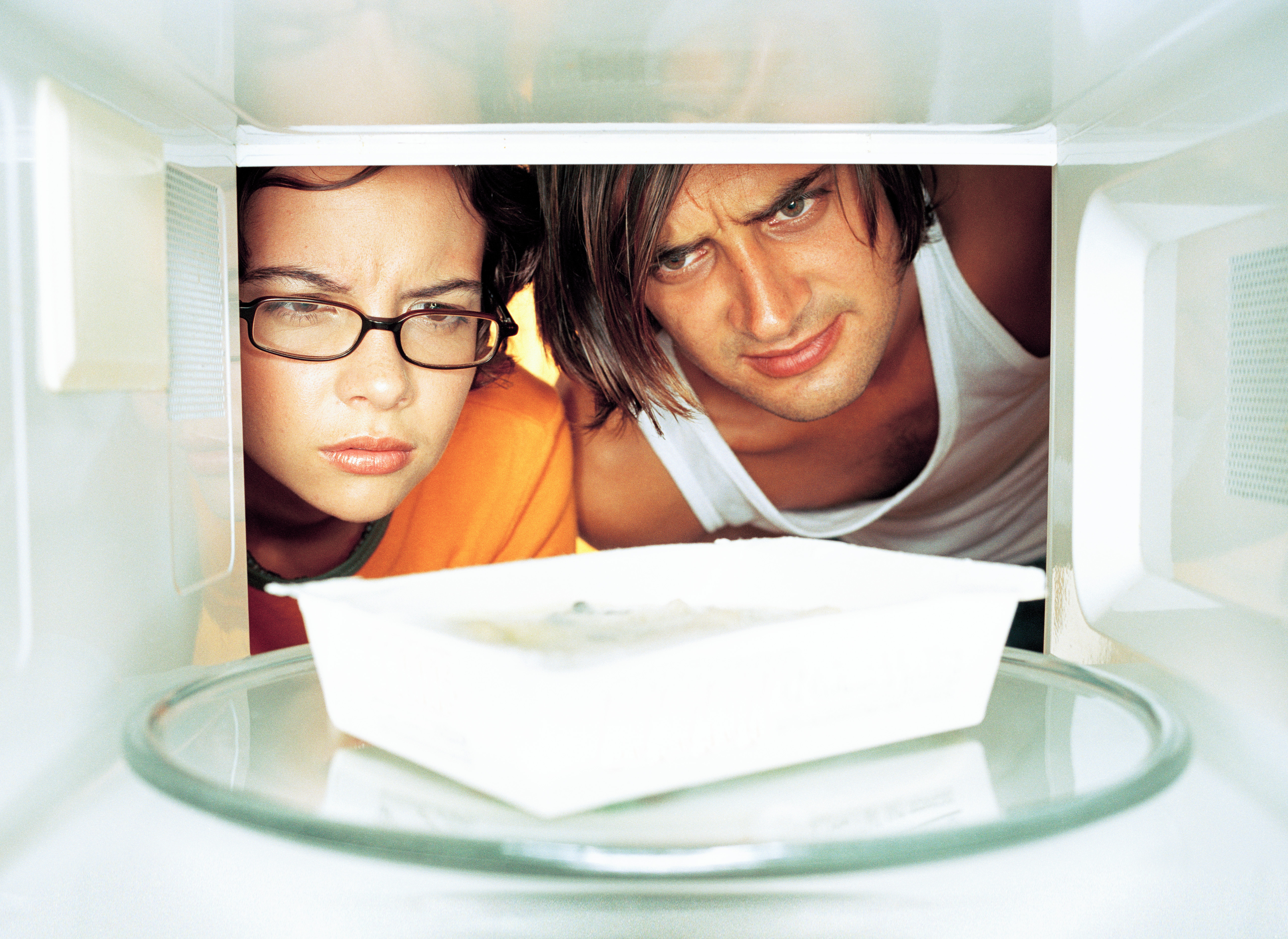 Young man and woman looking at microwave meal in microwave