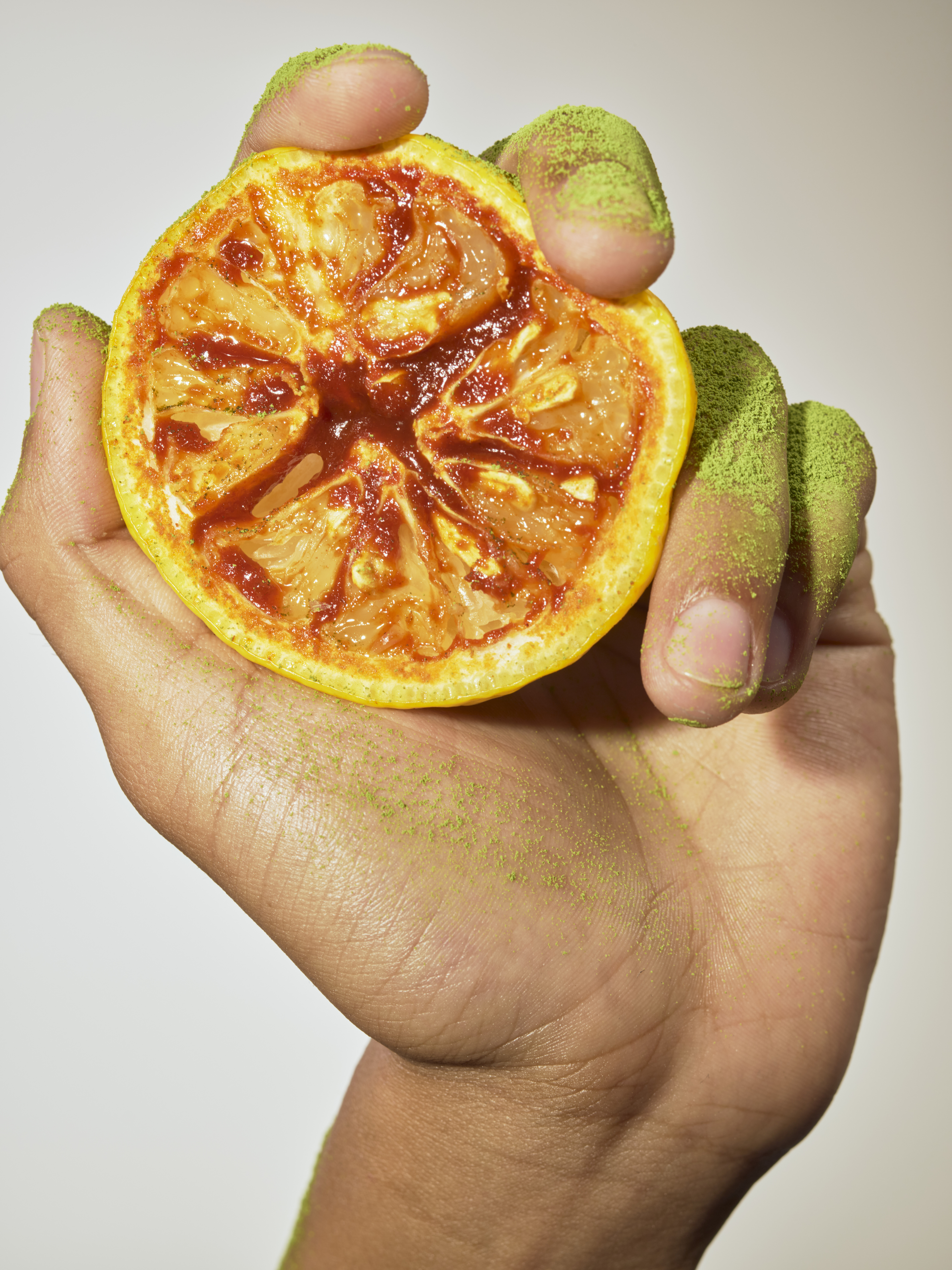 A hand dusted with matcha holding half a yuzu covered in gochujang. Food styled by Maggie Ruggiero. Photo / Grant Cornett, The New York Times