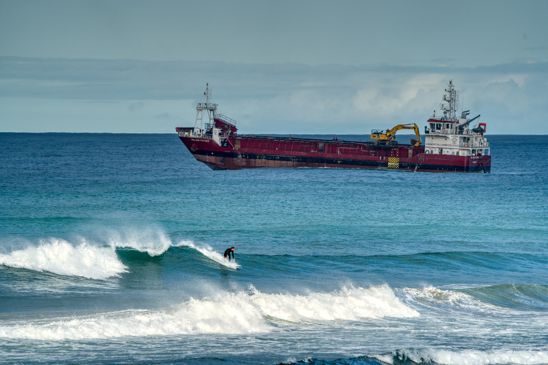 A surfer on the Pakiri coast is dwarfed by McCallum Bros' sand mining vessel which is at the centre of mulitple claims of ecological damage and consent breaches. Photo/ Doug Moores