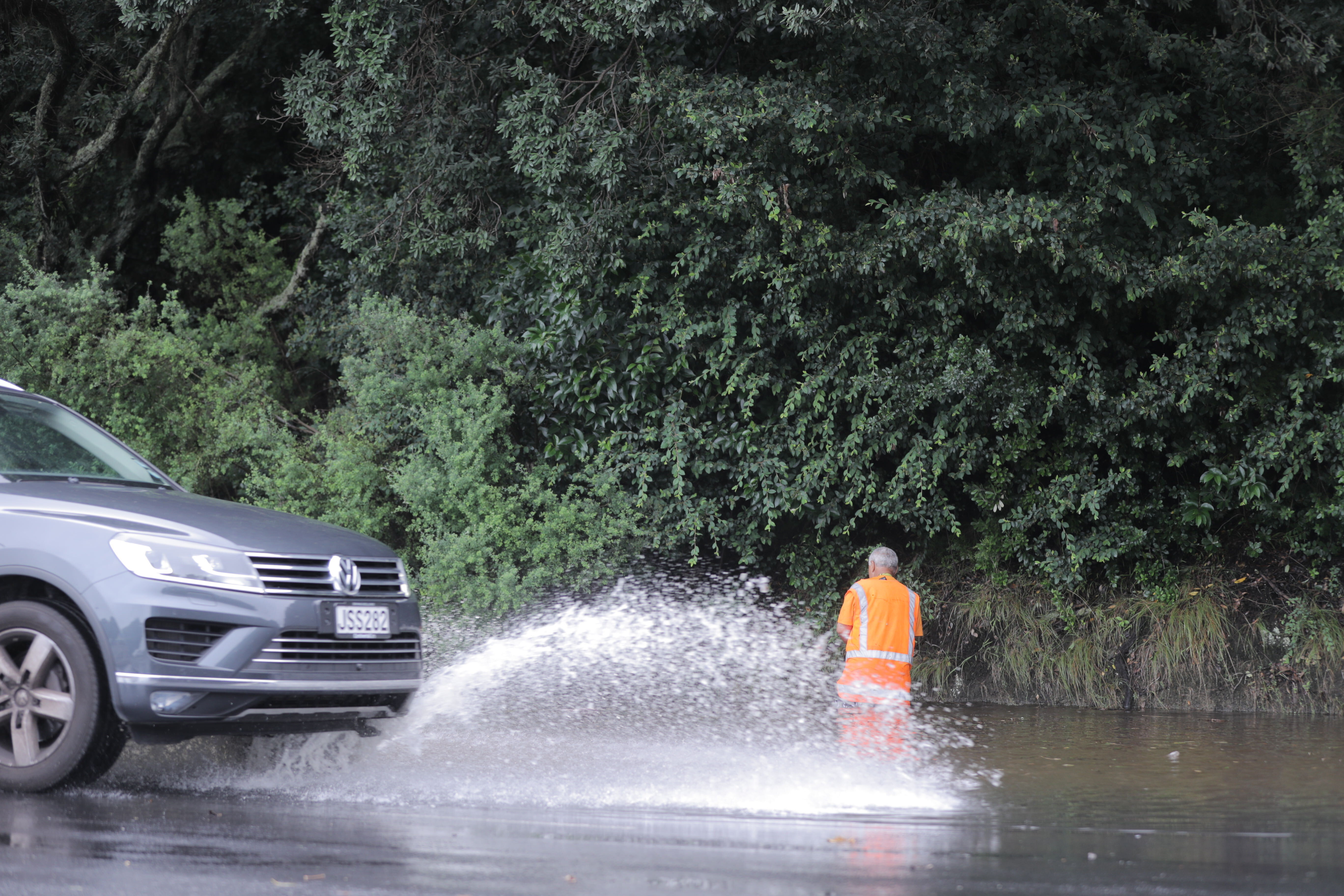 A road worker clears blocked drains causing flood on Tamaki Drive. Photo / Michael Craig