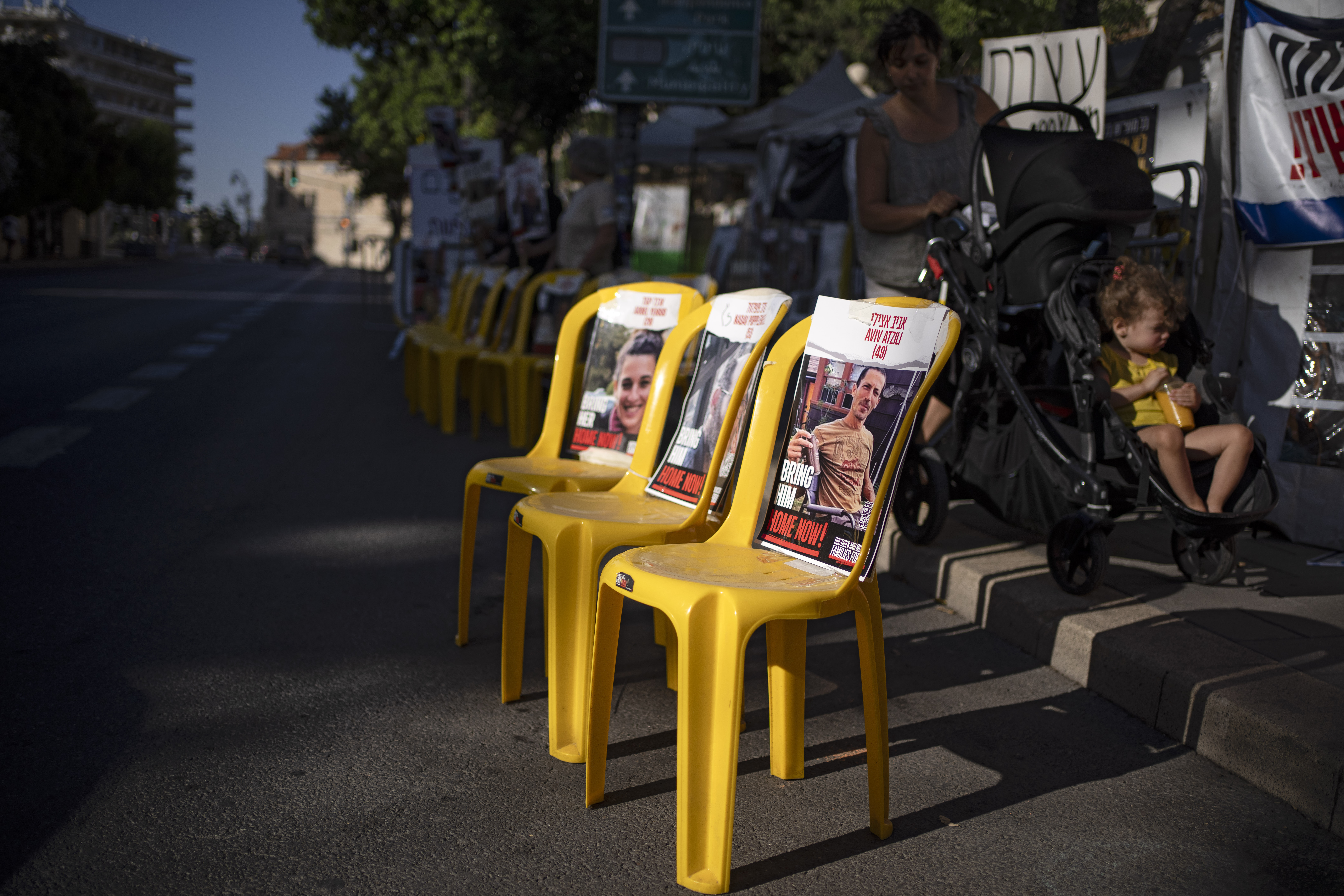 A woman pushes a baby trolley past empty chairs displaying photographs of hostages who were kidnapped during the October 7 Hamas cross-border attack in Israel, set on the street in Jerusalem. Photo / AP