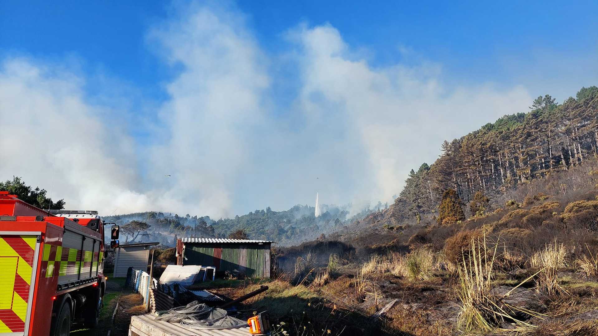 Firefighters, heavy machinery and helicopters are being used to fight a massive scrub fire that forced about 30 people to leave their homes. Photo / Paparoa Volunteer Fire Brigade
