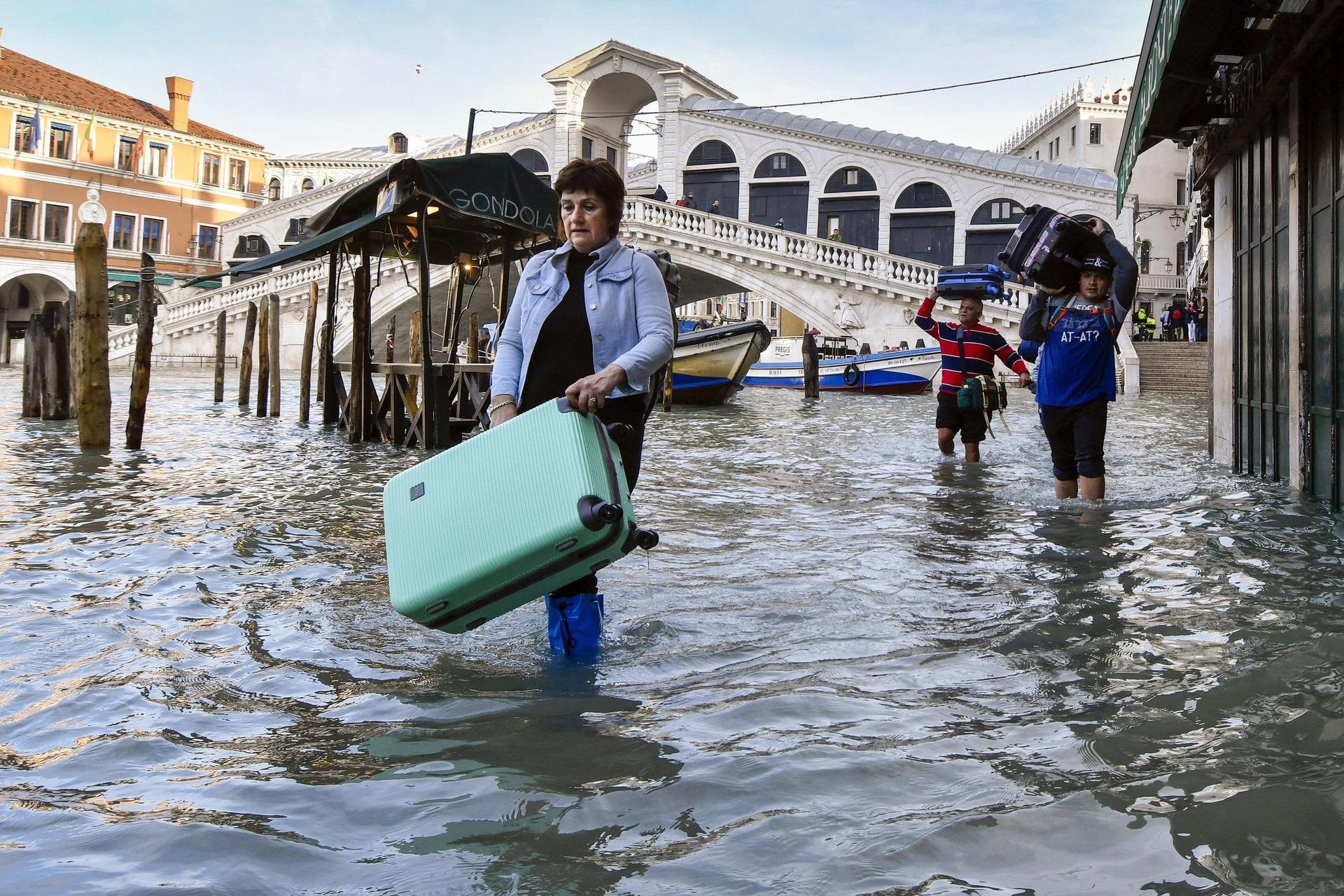 People carry their luggage as they wade through water during the city's second-worst flood in history in 2019. Photo / Luigi Costantini, AP Photo