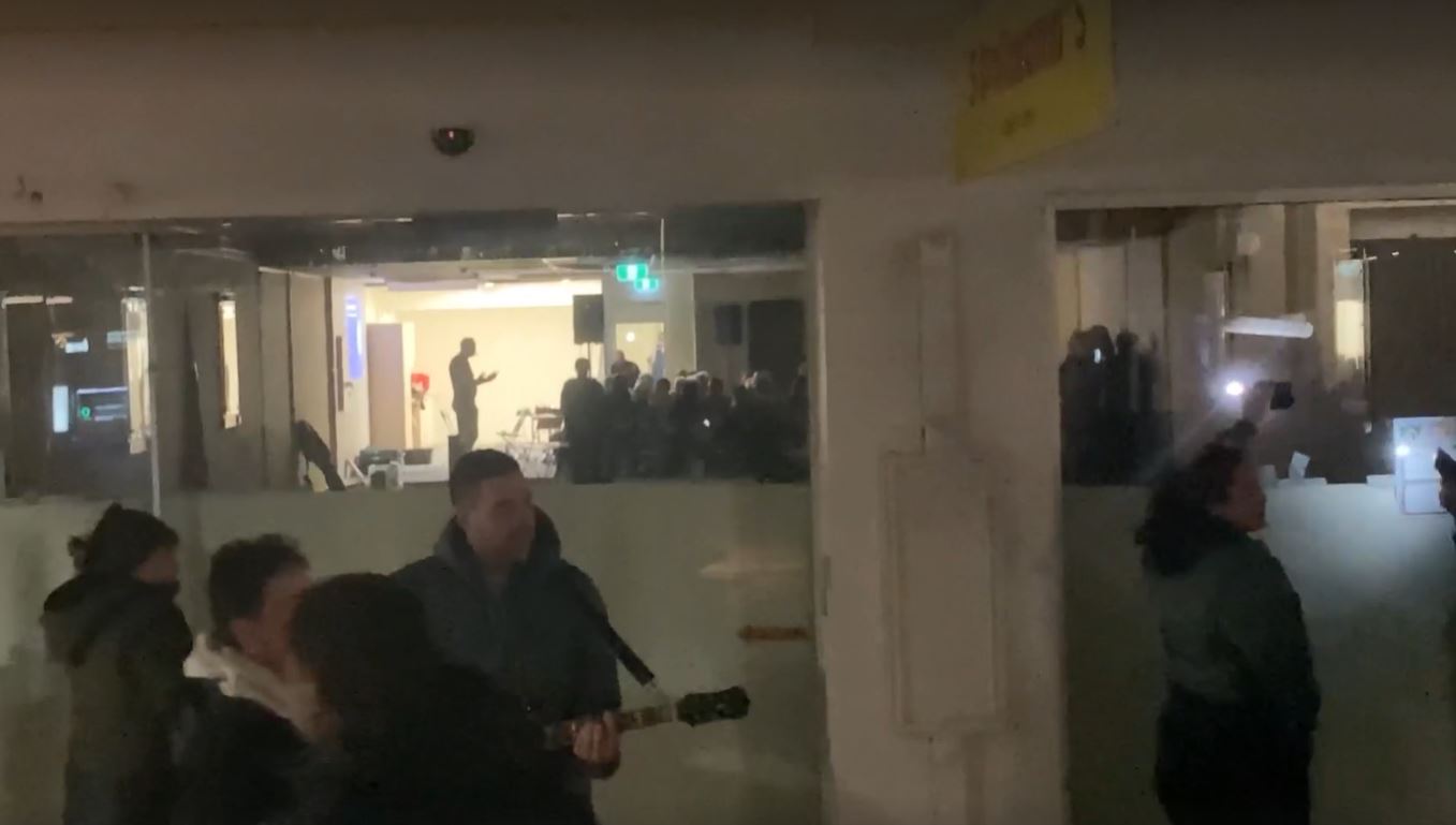 Julian Batchelor, silhouetted in the background, speaks to a Stop Co-Governance meeting in Hastings as protesters sing outside. Photo / Paul Taylor