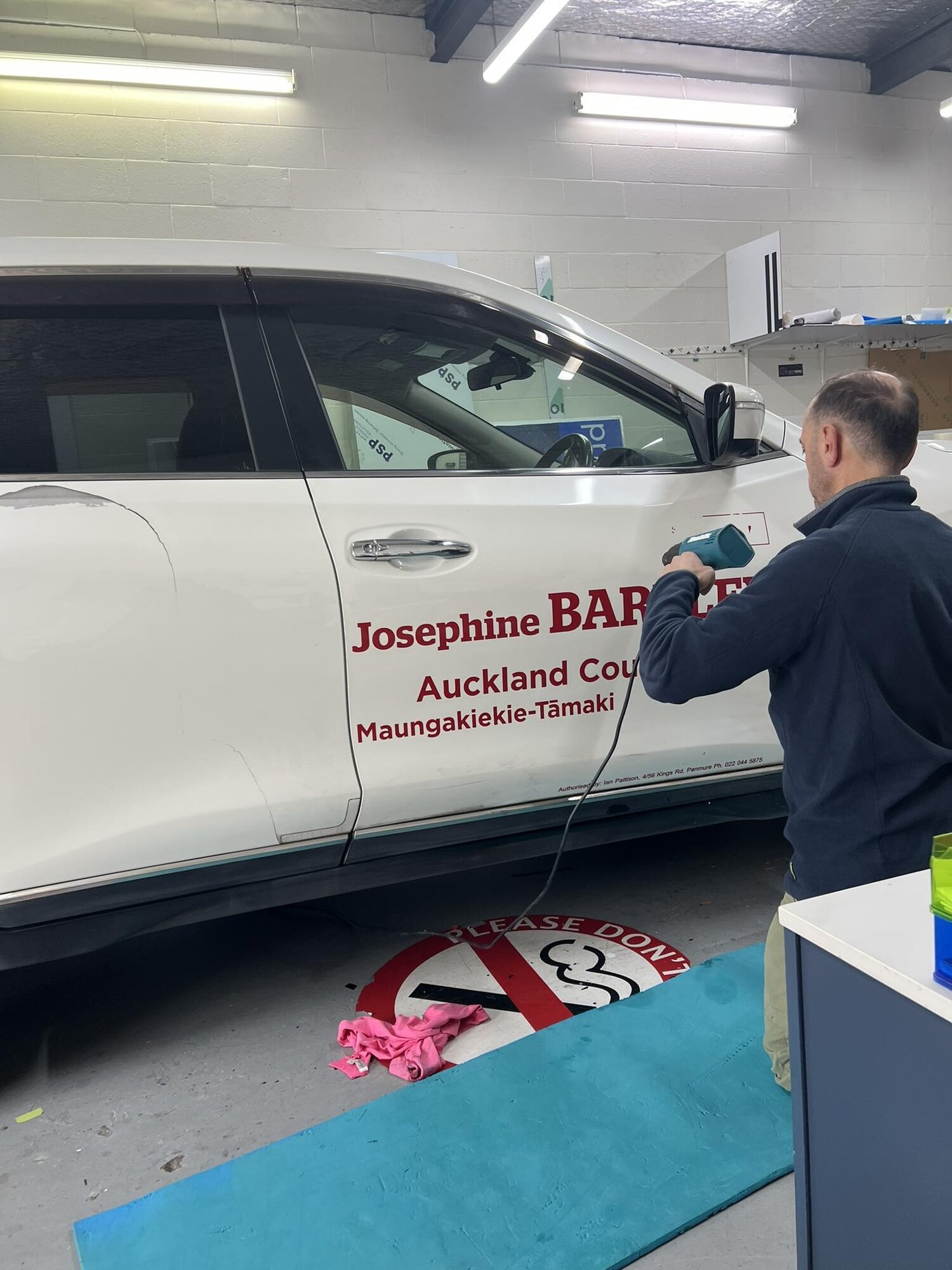 A tradesman removes the image and name of Auckland councillor Josephine Bartley from her car yesterday amid concerns for her safety. Photo / Josephine Bartley via Facebook