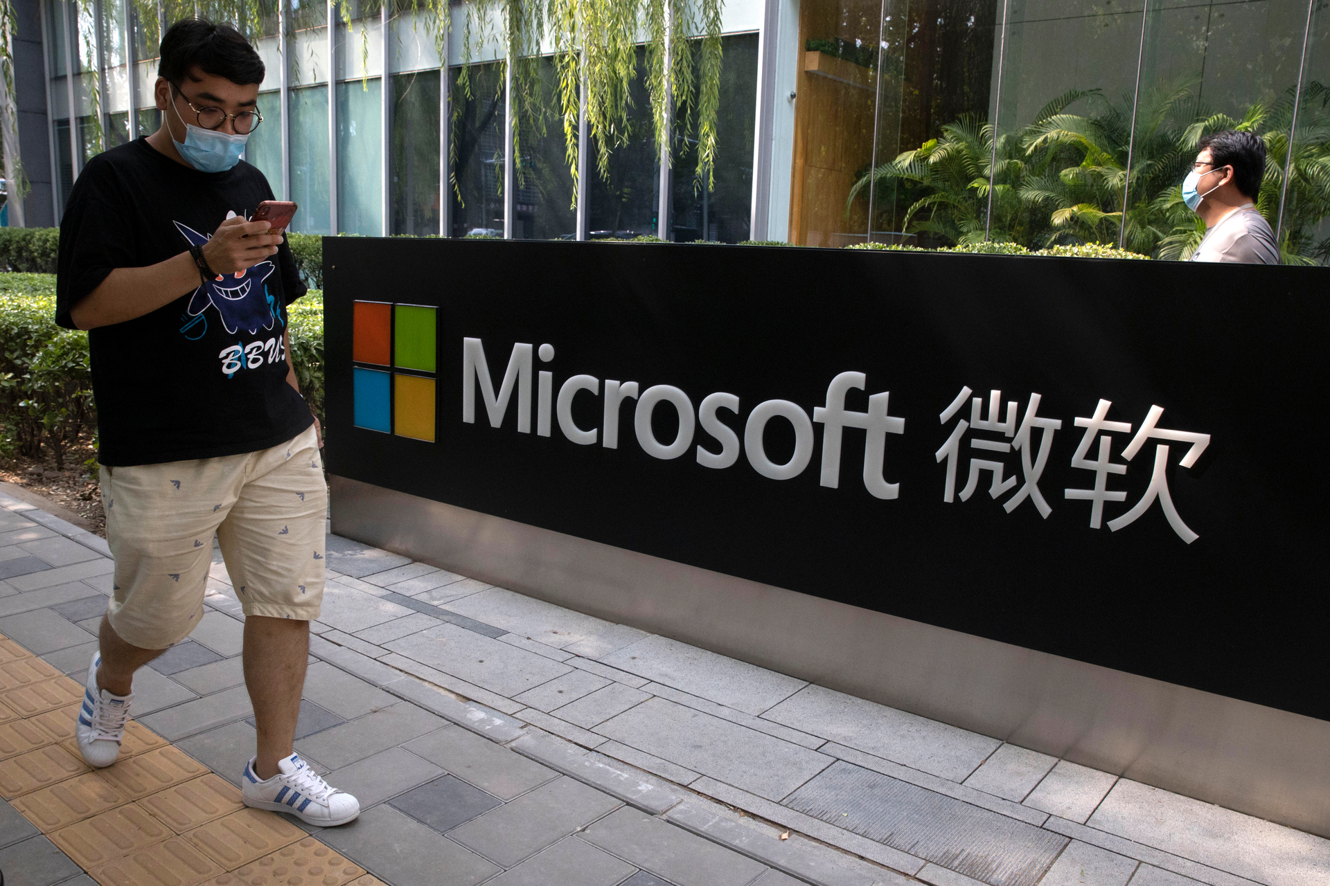 A man looks at his smartphone as he walks by the Microsoft office in Beijing, China. Photo / Ng Han Guan, AP, File