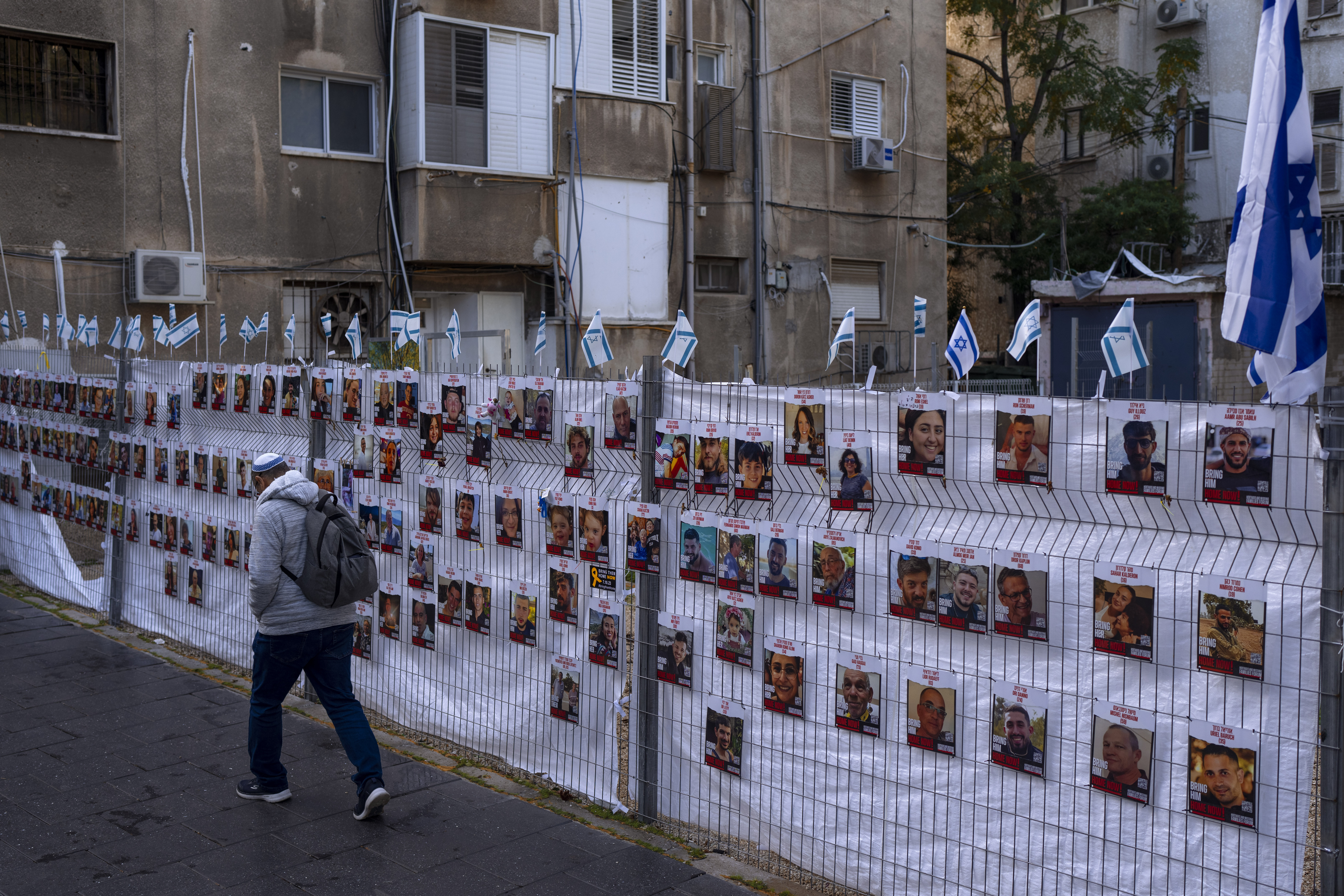 A man passes by a fence with photographs of hostages, mostly Israeli civilians who were abducted during the October 7, unprecedented Hamas attack. Photo / AP