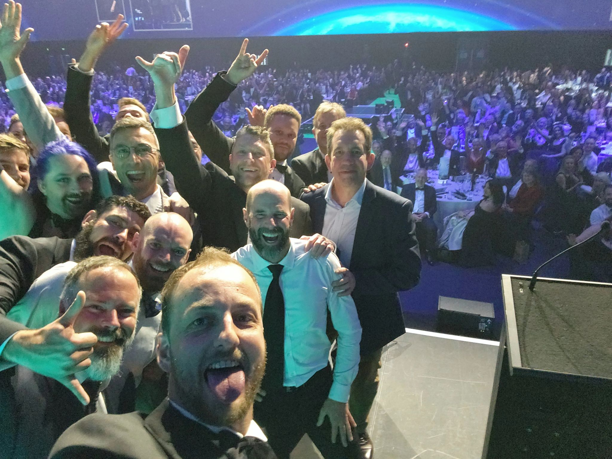 Syos's cofounder and CEO Samuel Vye (foreground) takes a selfie with his team from the Hi-Tech Awards 2025 stage. 