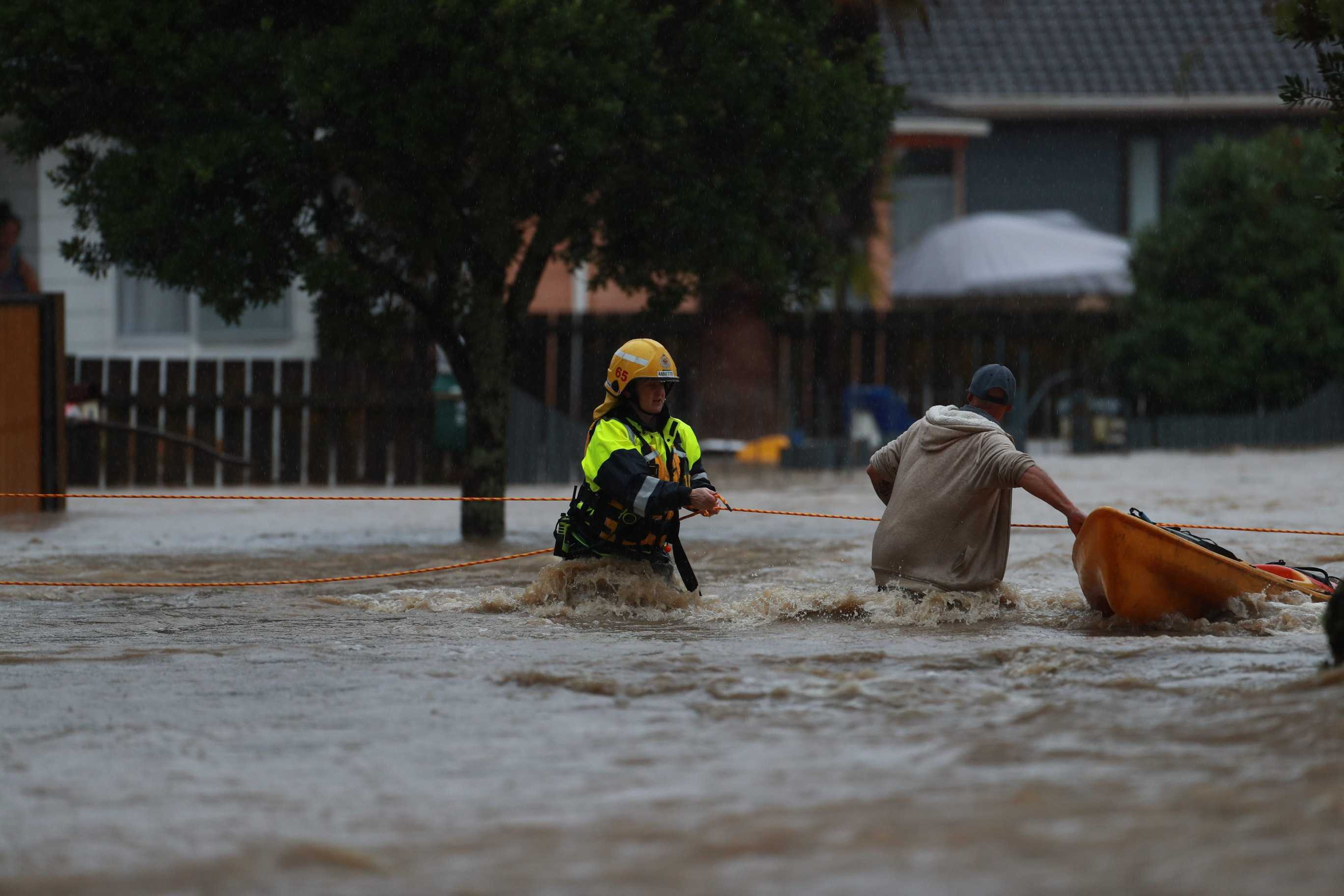 Firefighters use ropes to help rescue residents trapped by flooding in Urlich Drive, Ranui. Photo / Hayden Woodward