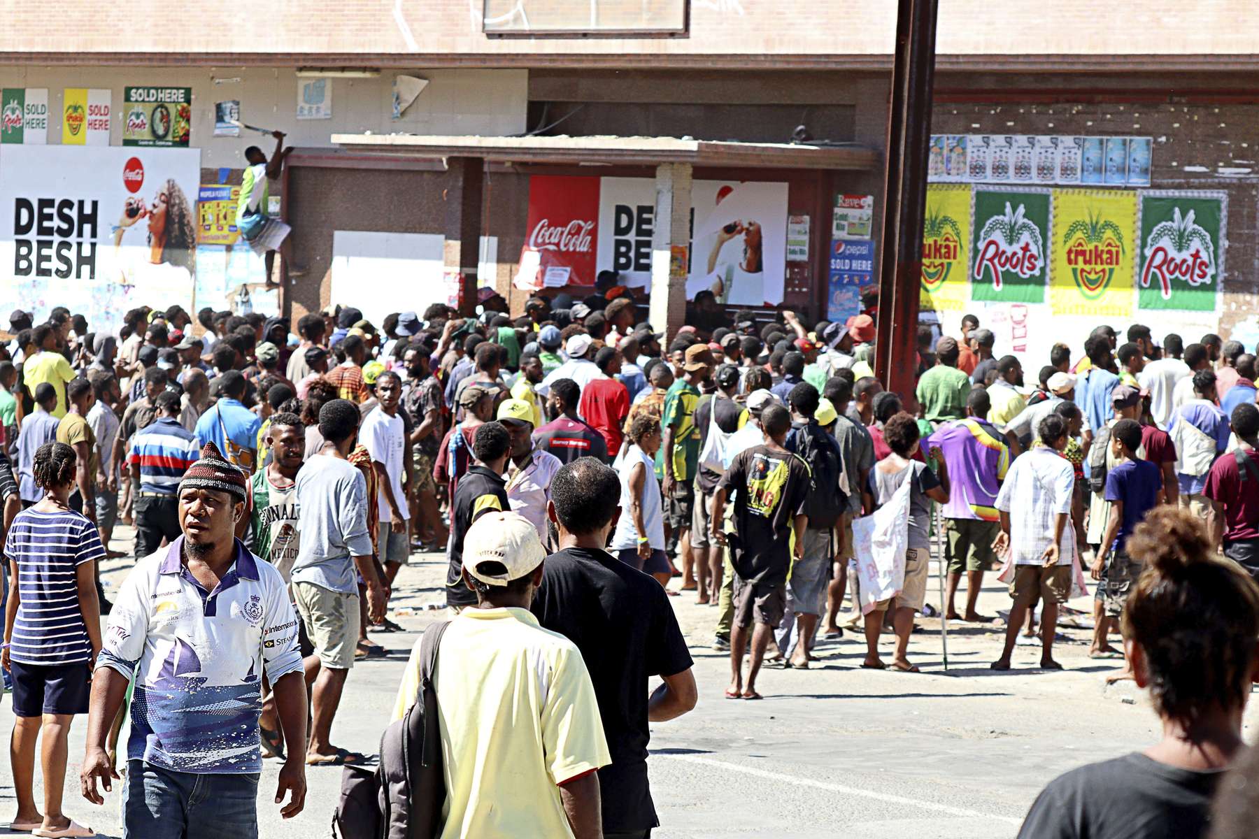 People gather at a closed shopping centre as a looter climbs (top left) in an attempt to gain access in Port Moresby, Papua New Guinea. Photo / Tarami Legei/Post Courier via AP