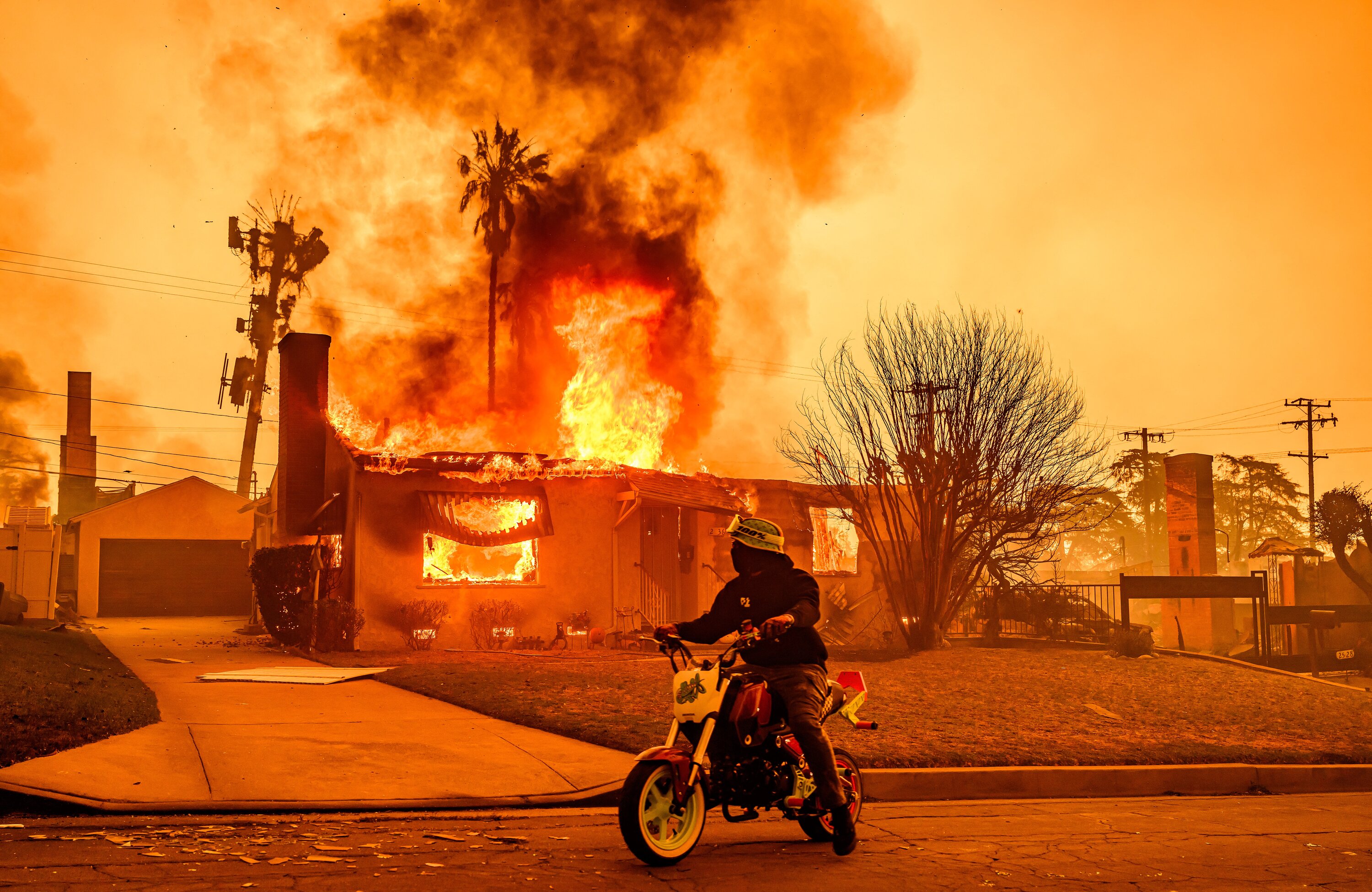 A motorcyclist stops to look at a burning home during the Eaton fire in the Altadena area of Los Angeles county. Photo / AFP