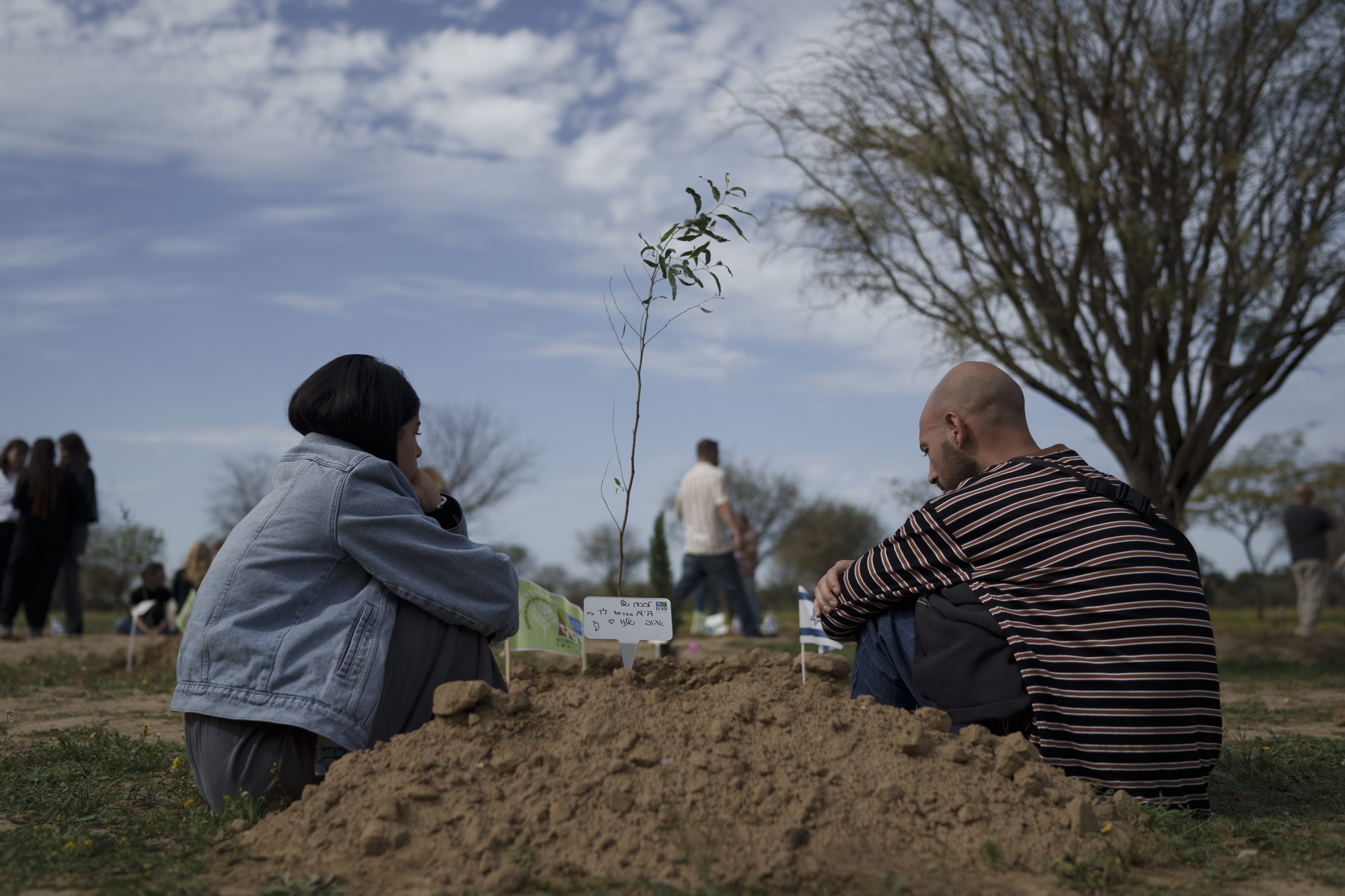 Friends and relatives sit next to a tree they planted in memory of a person who was killed at the Nova music festival in Re'im, Southern Israel. Photo / AP