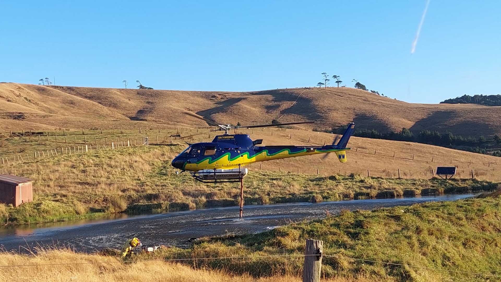 A helicopter with a monsoon bucket fills up water to fight the scrub fire in Aranga.
Photo / Supplied