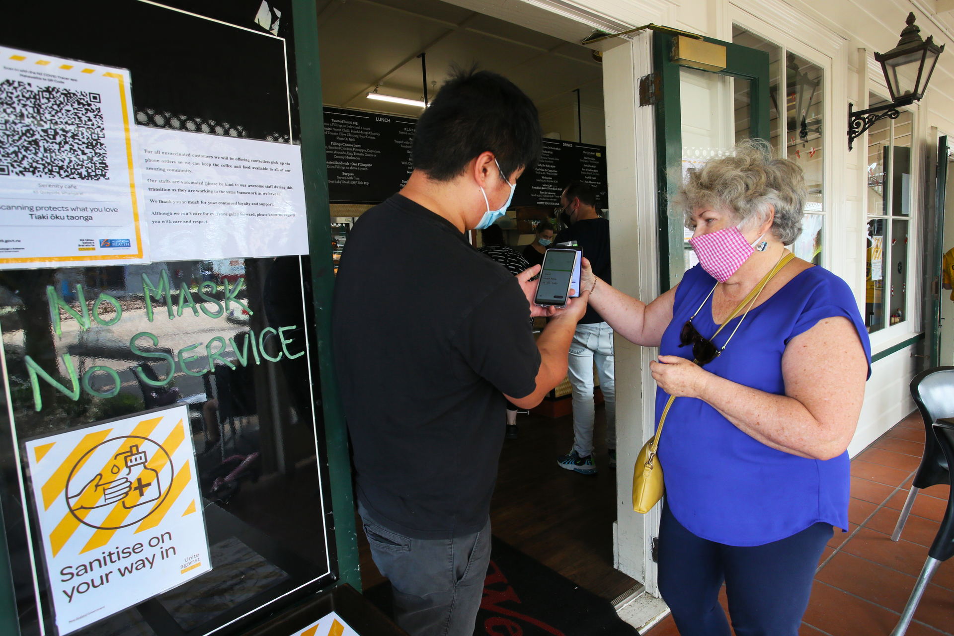Businesses get to grips with the traffic light system. Alfred Hong, owner of Serenity Cafe, checks Linda Ward's vaccine passport. Photo / Tania Whyte