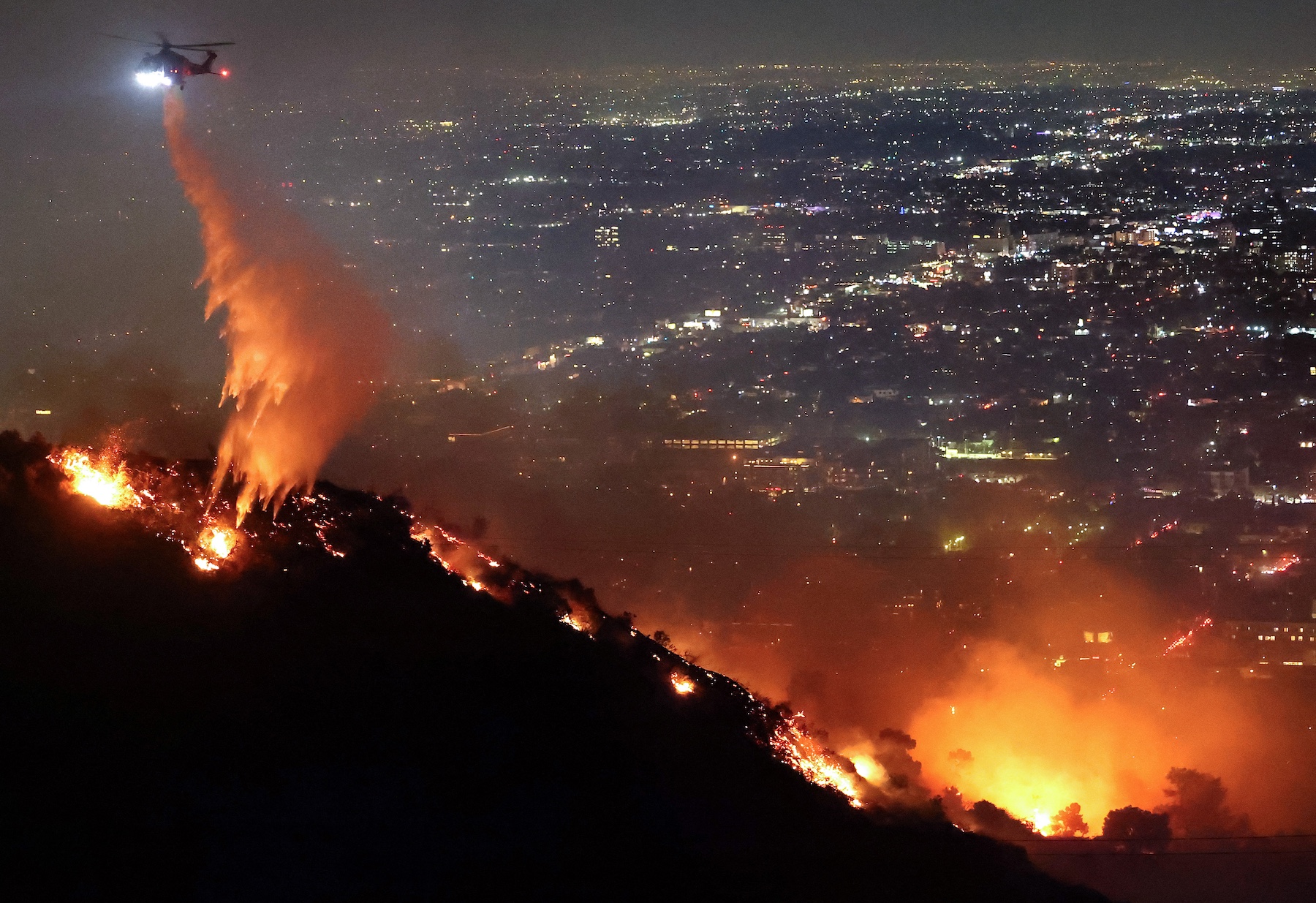 A firefighting helicopter drops water as the Sunset Fire burns in the Hollywood Hills. Photo / AFP