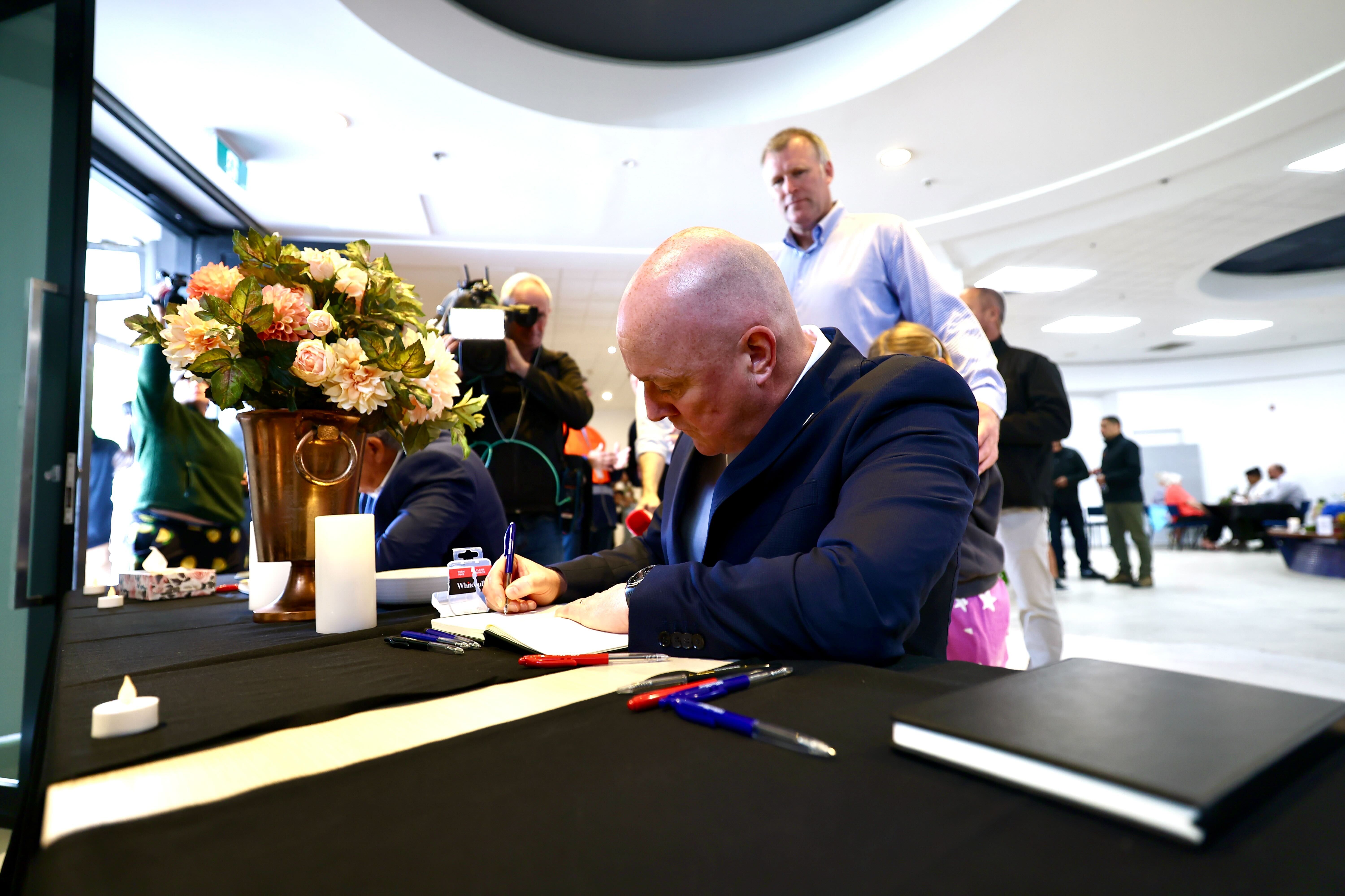 Prime Minister Christopher Luxon signs a book provided at a community centre erected after the Mount Maunganui landslide. Photo / Dean Purcell