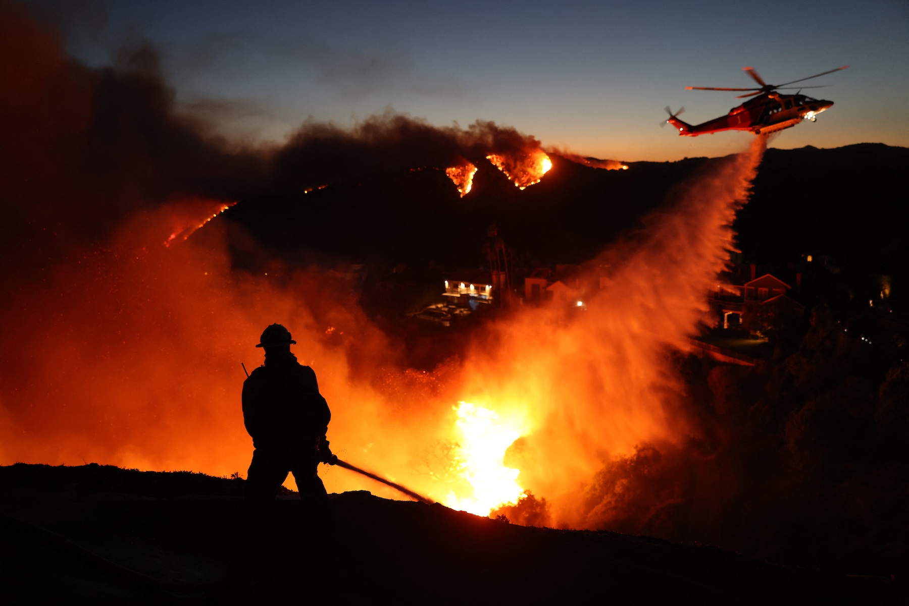 Fire personnel respond to homes destroyed while a helicopter drops water as the Palisades Fire grows in Pacific Palisades, California, on January 7. Photo / AFP