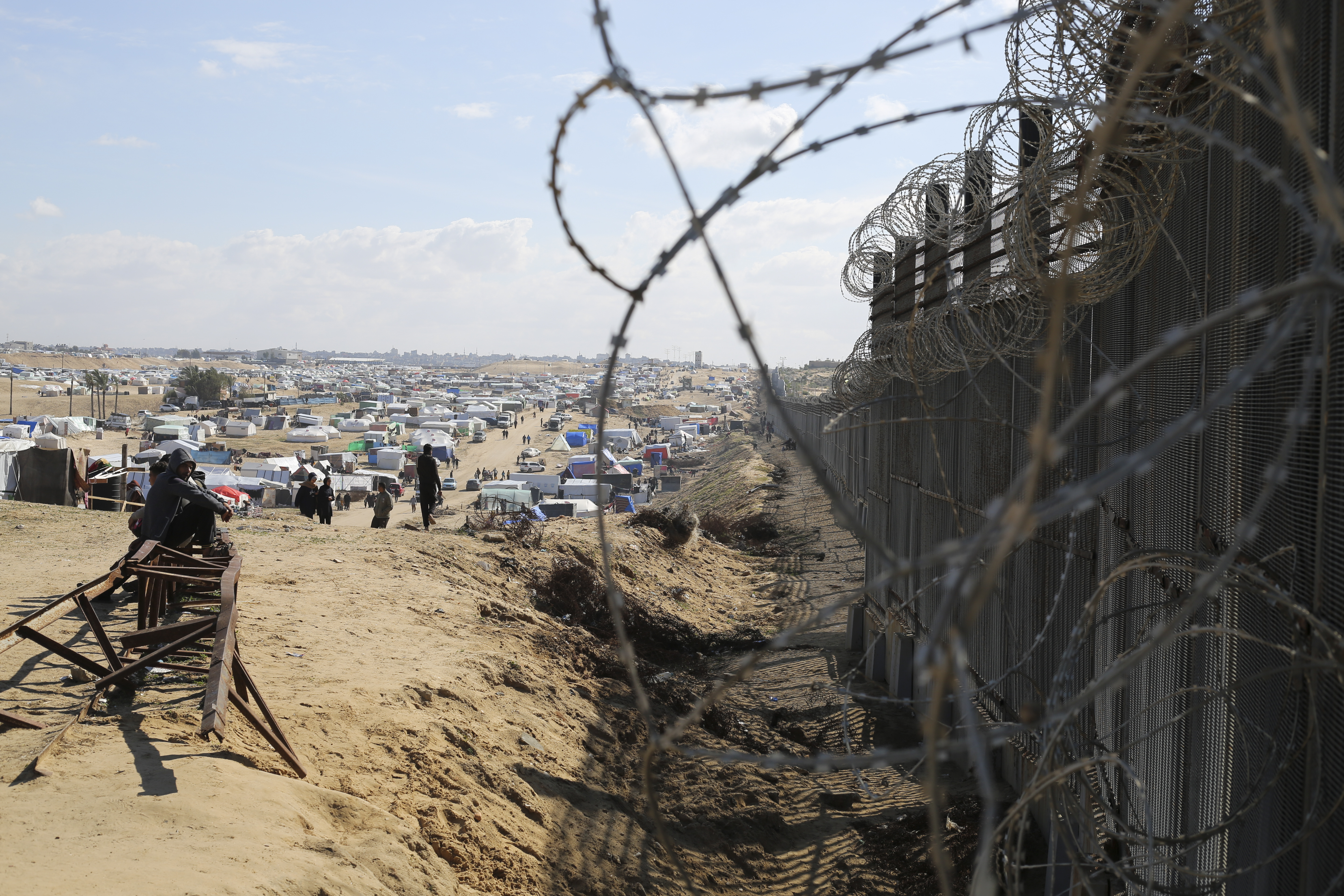 Palestinians displaced by the Israel air and ground offensive on the Gaza Strip sit next to the border fence with Egypt in Rafah. Photo/ AP