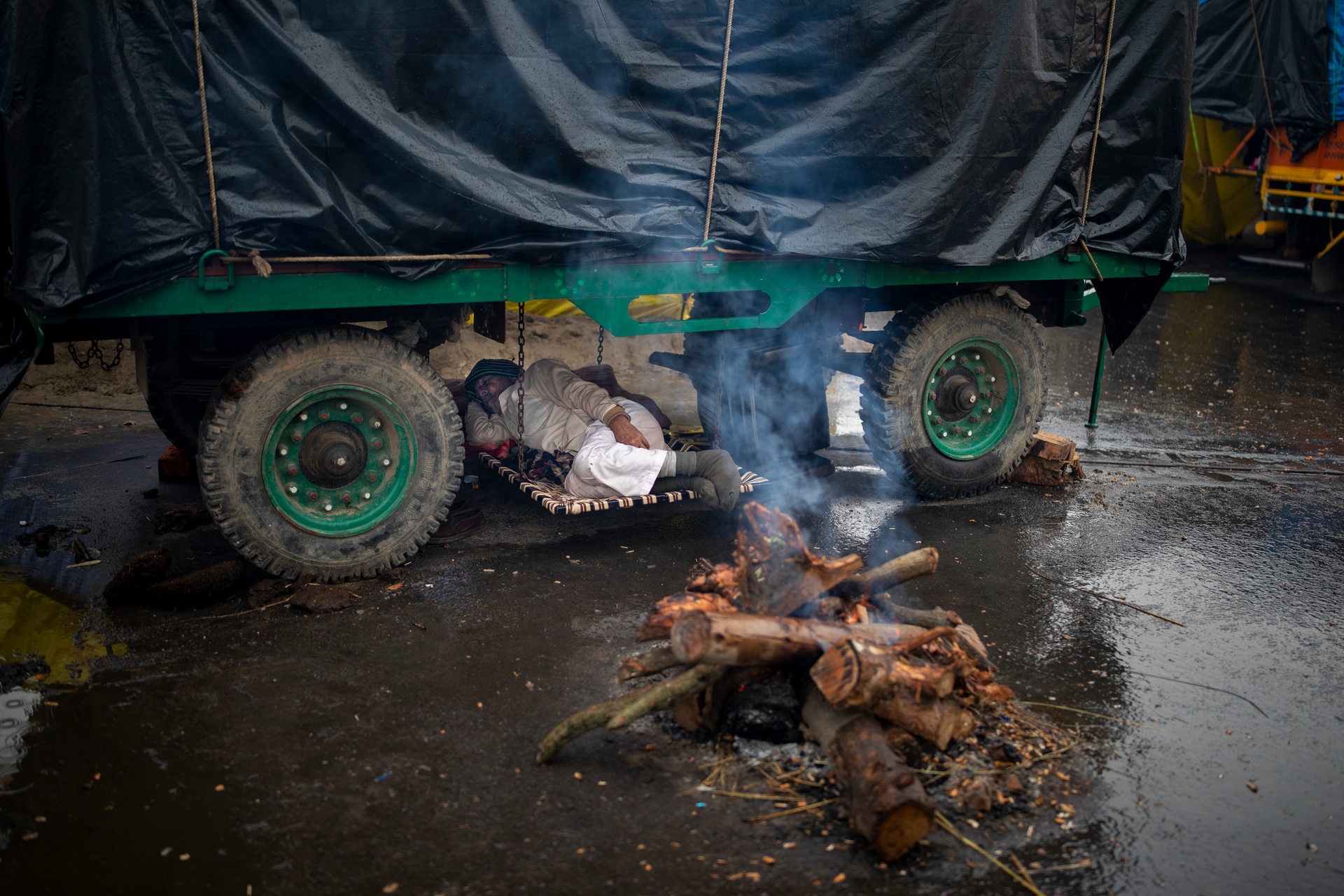 A farmer lies under the belly of a tractor trolley next to a bonfire as they battle the conditions of sleeping on the streets while protesting. Photo / AP