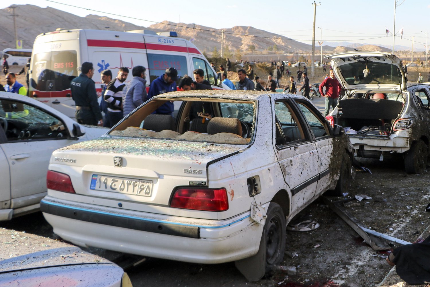 People stay next to destroyed cars after an explosion in Kerman, Iran, on Wednesday, January 3. Iran says bomb blasts at an event honouring a prominent Iranian general slain in a US airstrike in 2020 have killed at least 103 people and wounded 188 others. (Tasnim News Agency via AP)