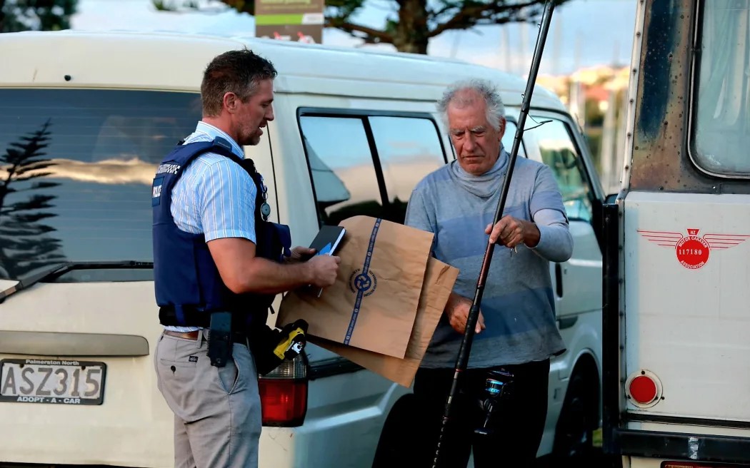 Fisherman Paul Middleton talking to police after fishing out human remains wrapped in plastic bags in Gulf Harbour. Photo / Nick Monro, RNZ