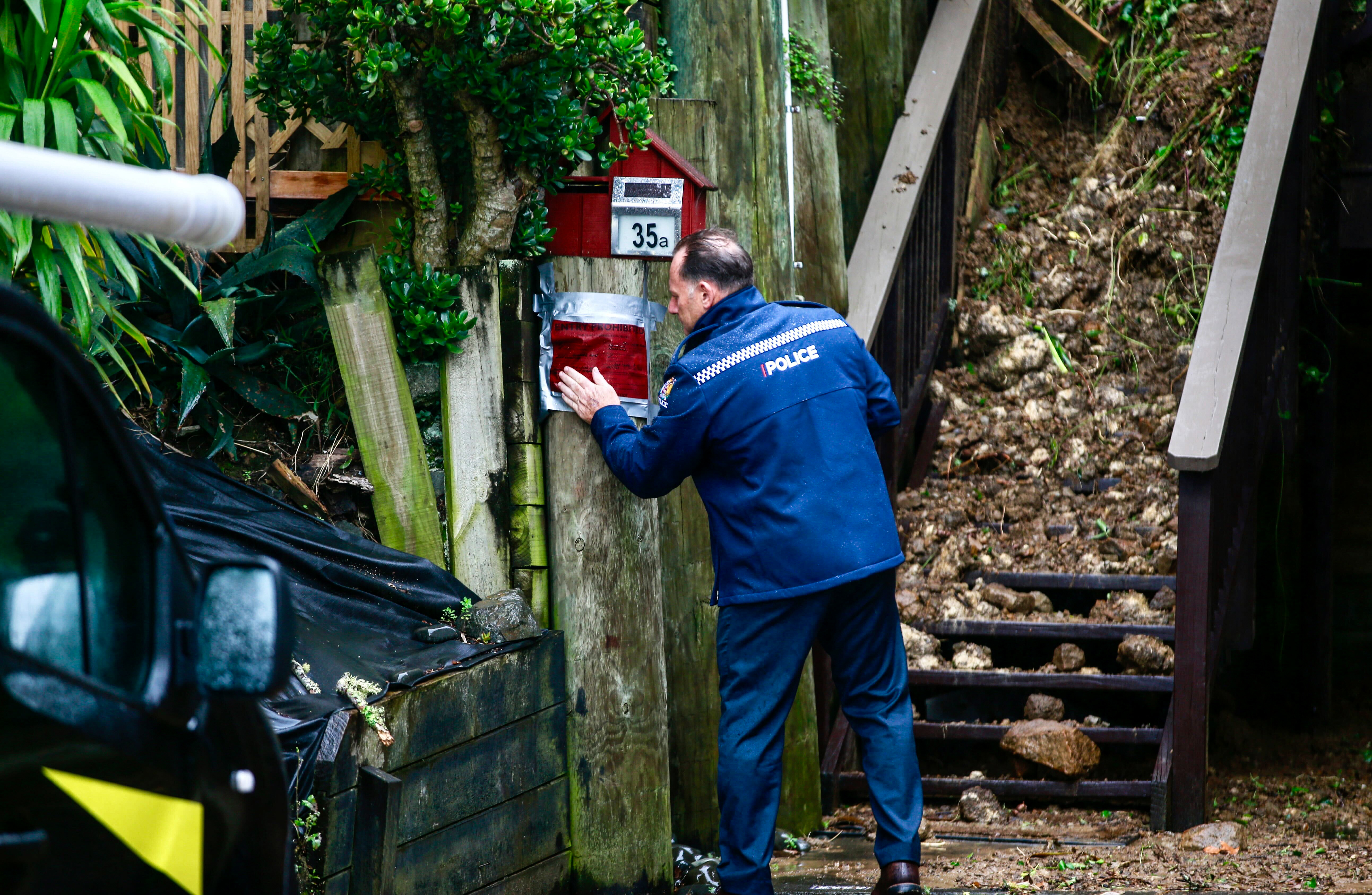 A police officer places a red sticker on a house on Shore Rd, Remuera, after heavy rain caused landslips and widespread destruction across the Auckland Region. Photo / Alex Burton