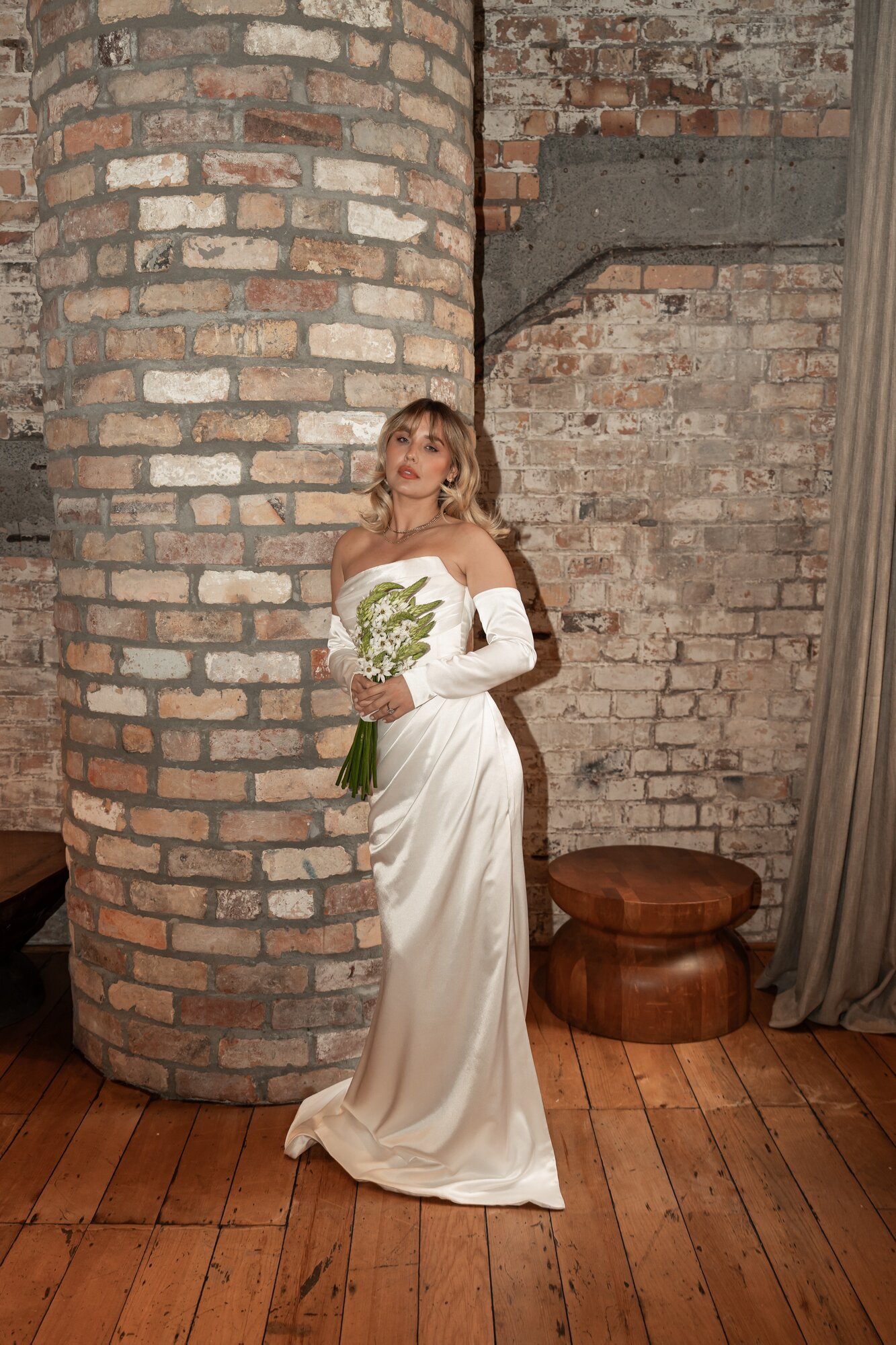 Jazmyne Aria wears the Rochel: 'A structured, off-shoulder bodice with controlled draping and long sculpted sleeves flows into a fluid satin column, opened by a bold front slit.' Photo / Supplied