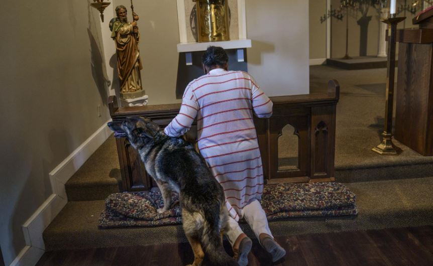 Tanya Britton prays with her dog, Sybil, by her side, while helping to prepare for Mass at St James Catholic Church. Photo / AP