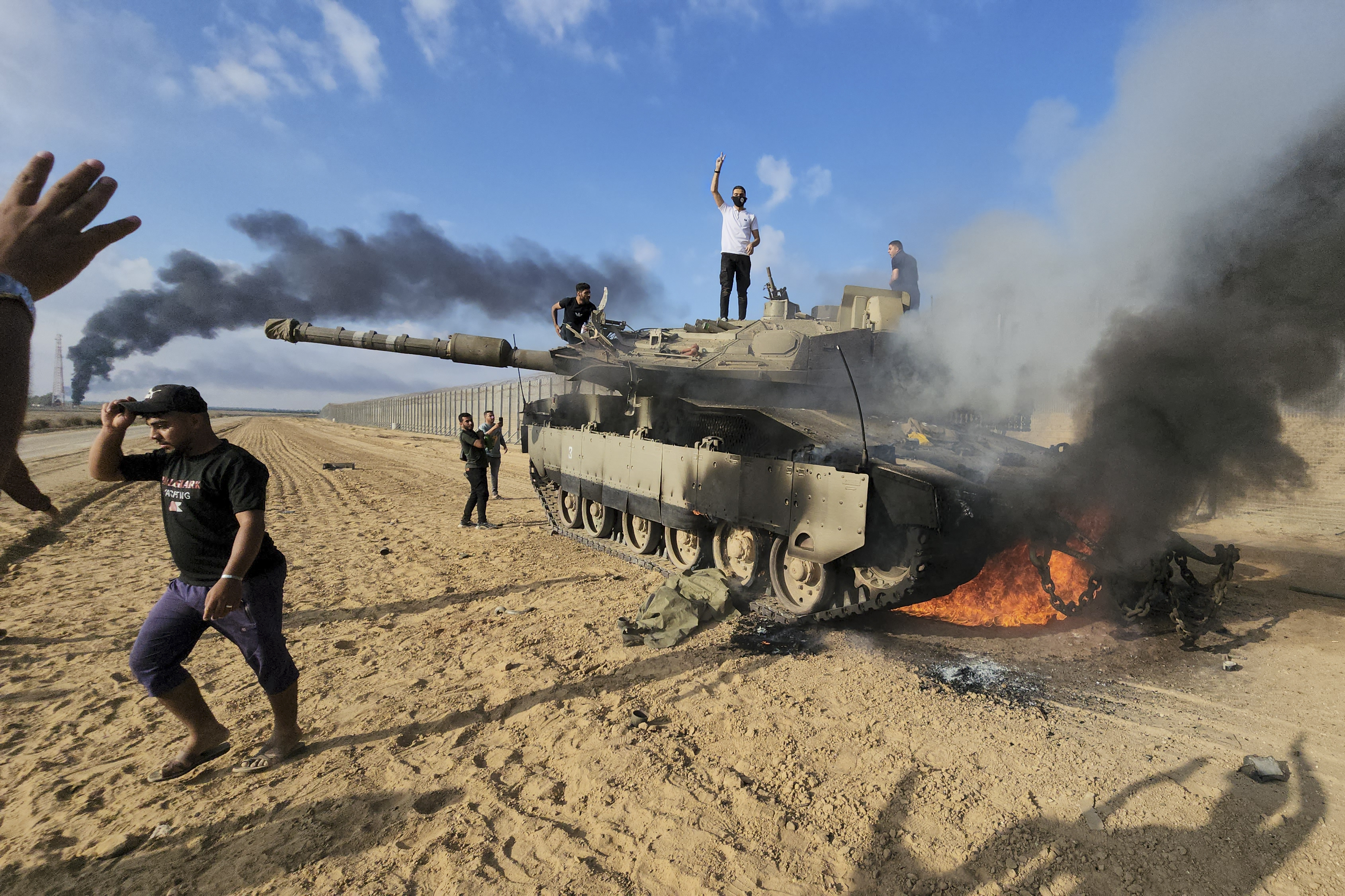 Palestinians celebrate next to a destroyed Israeli tank at the border fence between Israel and the Gaza Strip, east of Khan Younis, during a surprise attack on Israel. Photo / AP