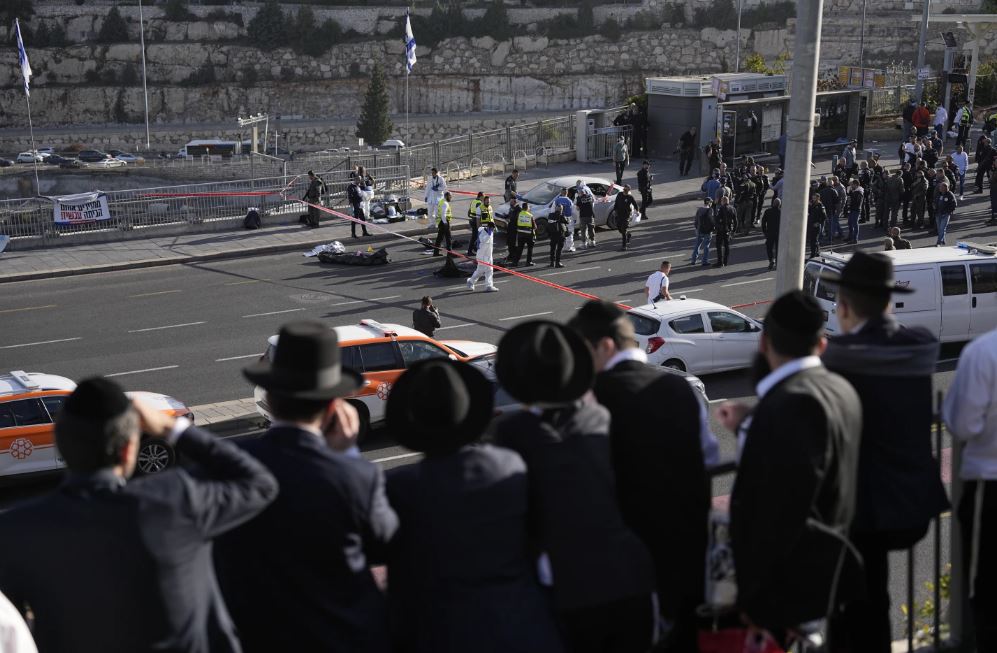 People look at Israeli police officers and volunteers from the Zaka rescue service work at the shooting attack in Jerusalem. Photo / AP