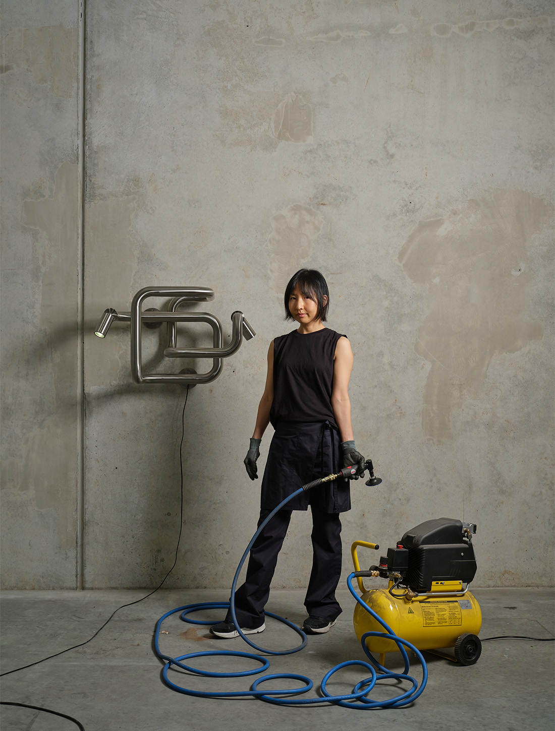 Yona Lee, 2025, studio portrait, pictured with ‘Light in Transit’, 2025, Stainless steel, lamps, 47.5 x 80 x 43.5cm. Courtesy the artist and Fine Arts, Sydney. Photo / Sam Hartnett
