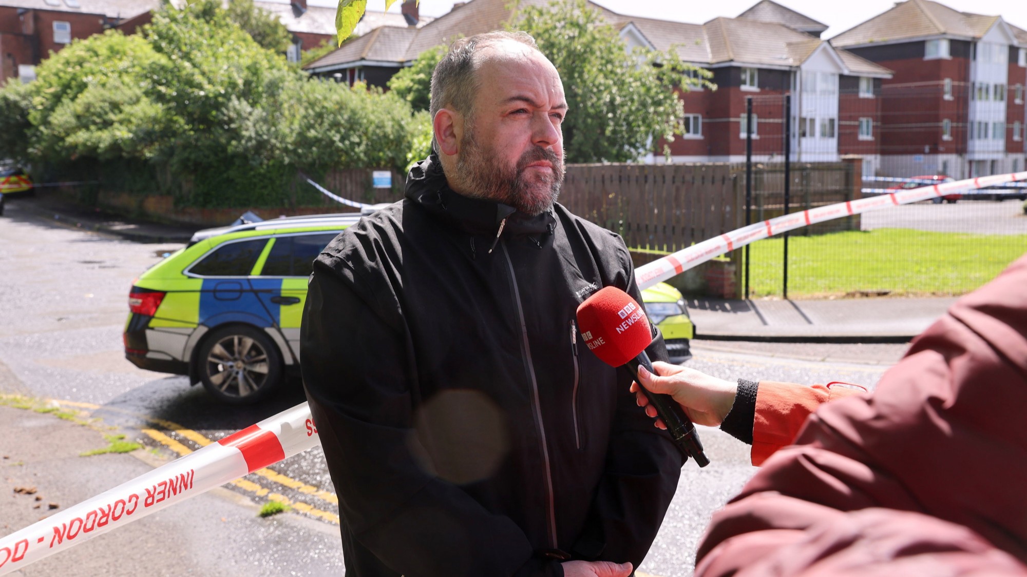 Belfast City Council Councillor Paul McCusker speaking to members of the media near to the scene of a stabbing outside apartments in north Belfast.