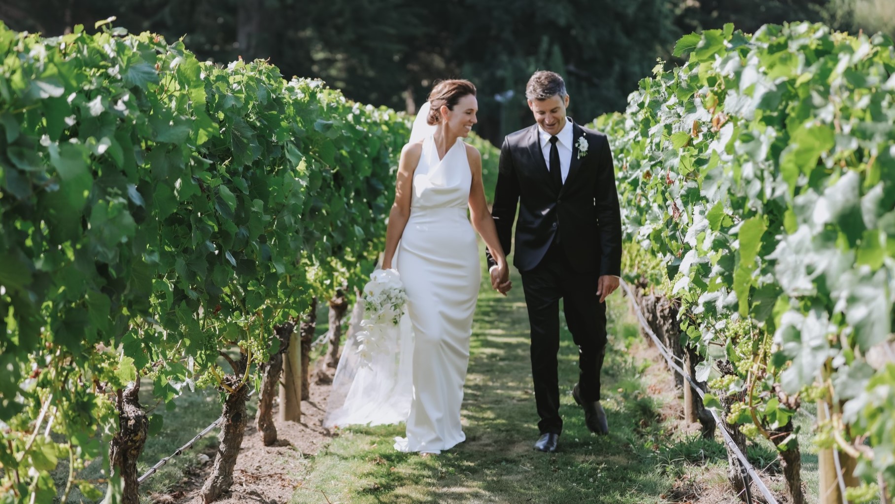 Newlyweds Dame Jacinda Ardern and Clarke Gayford walk through a vineyard.
