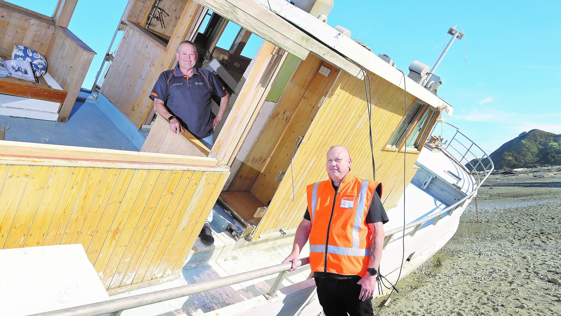A photo of Auckland city council workers inspecting a derelict boat on a beach.