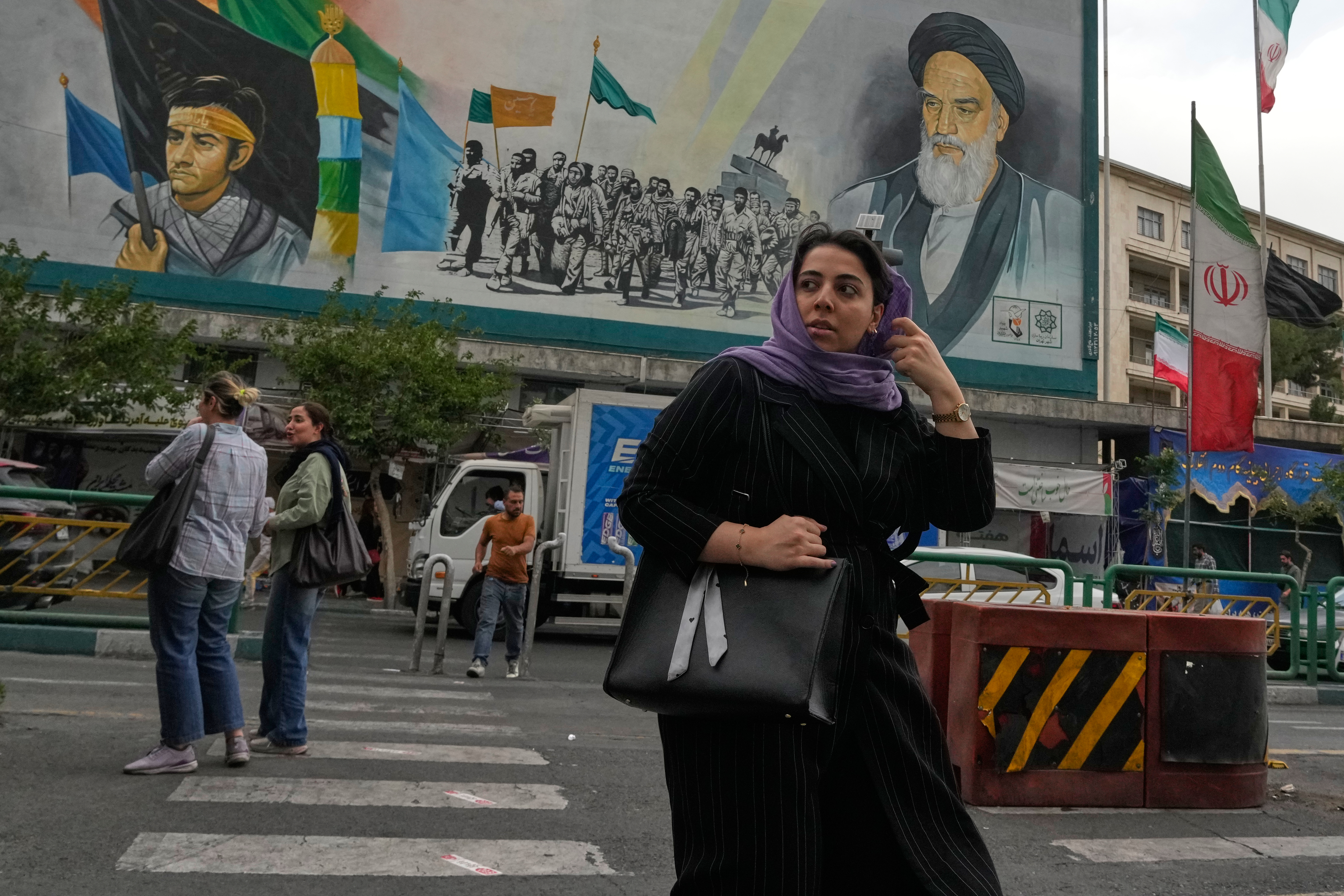 A woman crosses a street in front of a painting of the late Iranian revolutionary founder Ayatollah Khomeini and paramilitary Basij forces in downtown Tehran, Iran, Sunday, May 24, 2026.