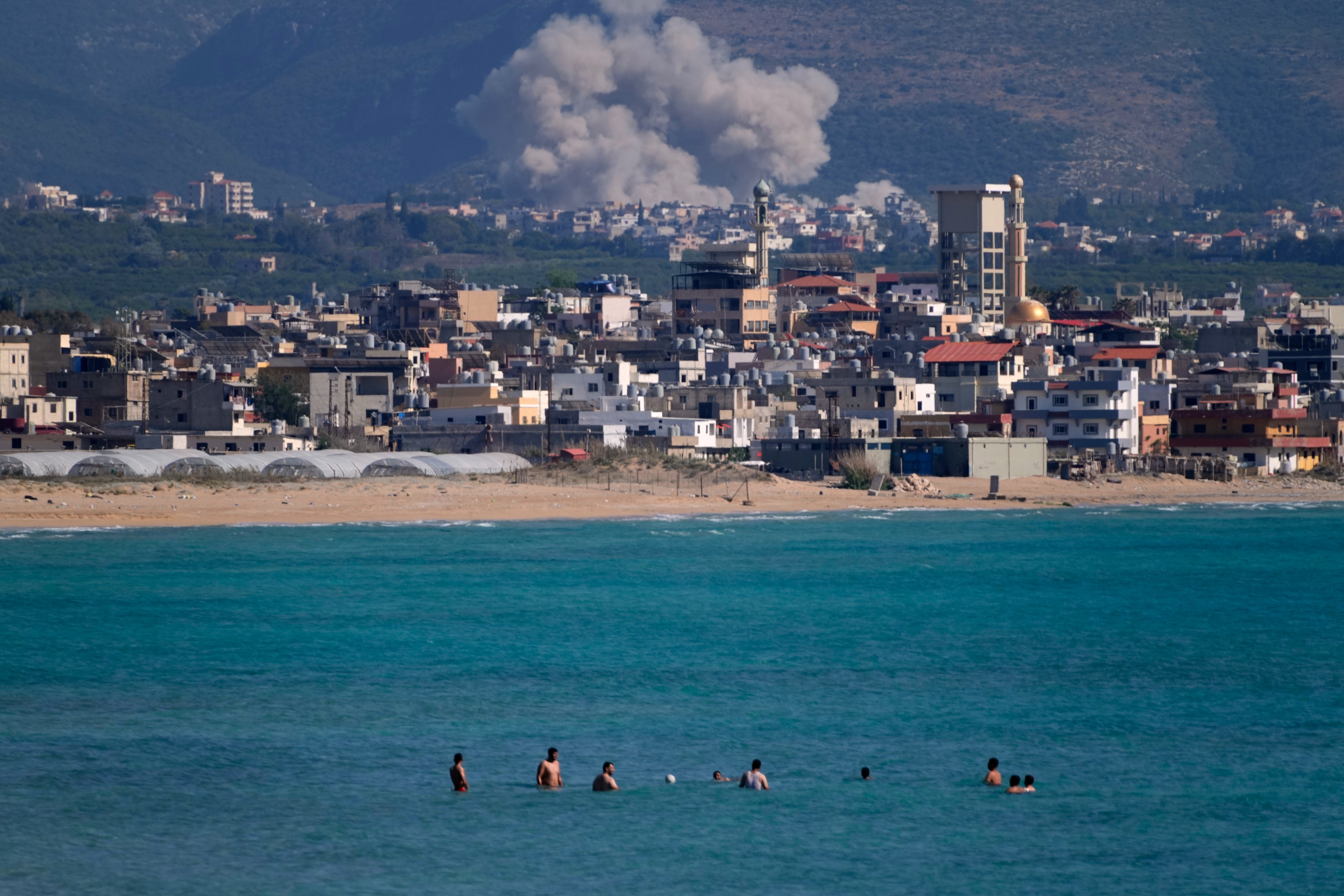People swim on a public beach as smoke, background, rises from an Israeli airstrike that hit the Qlaileh village, seen from the southern port city of Tyre, Lebanon, Tuesday, June 2, 2026. 
