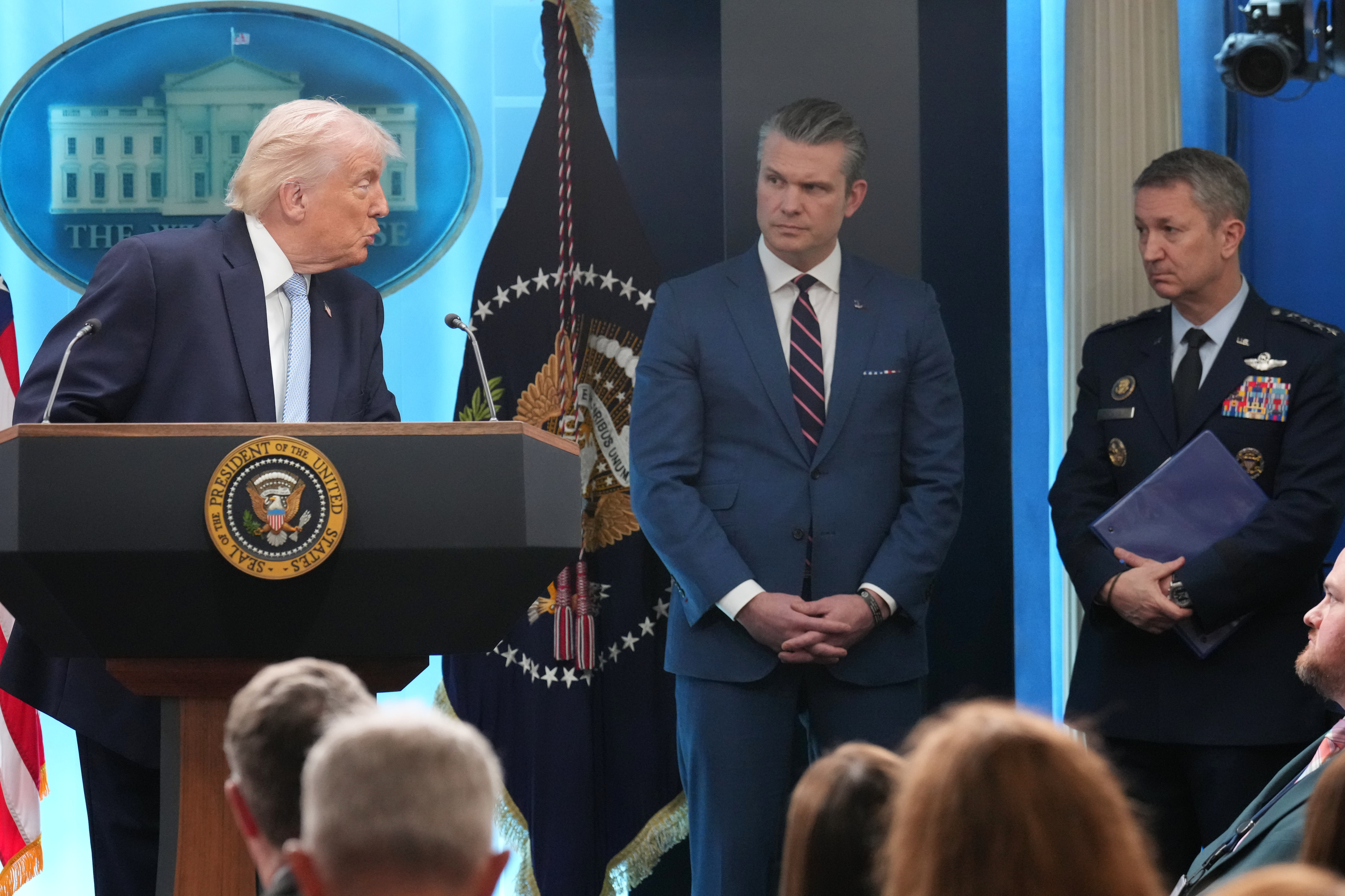 President Donald Trump looks to Defense Secretary Pete Hegseth and Chairman of the Joint Chiefs of Staff Gen. Dan Caine as he speaks with reporters during a news conference