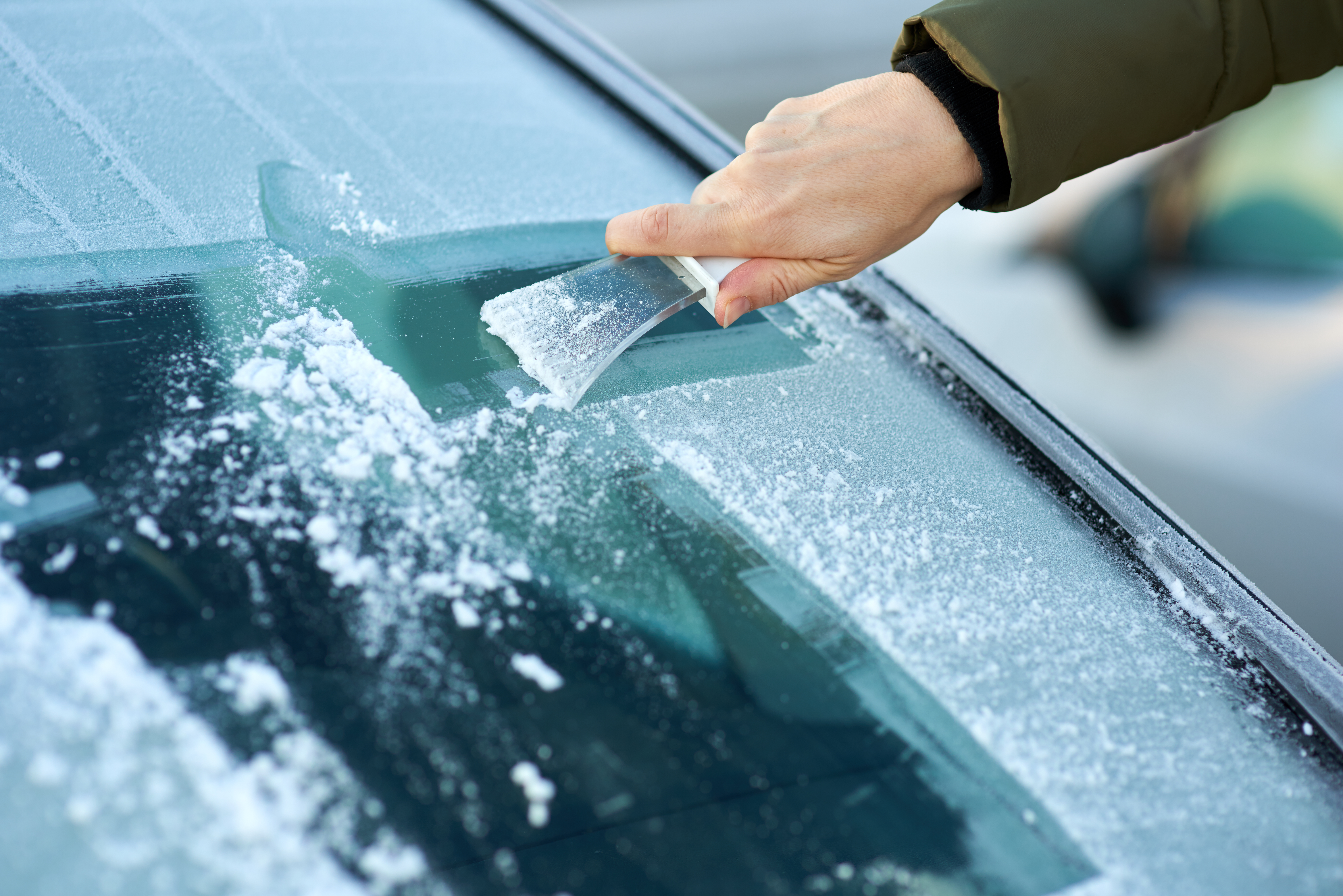 A person scrapes ice off a car windscreen.