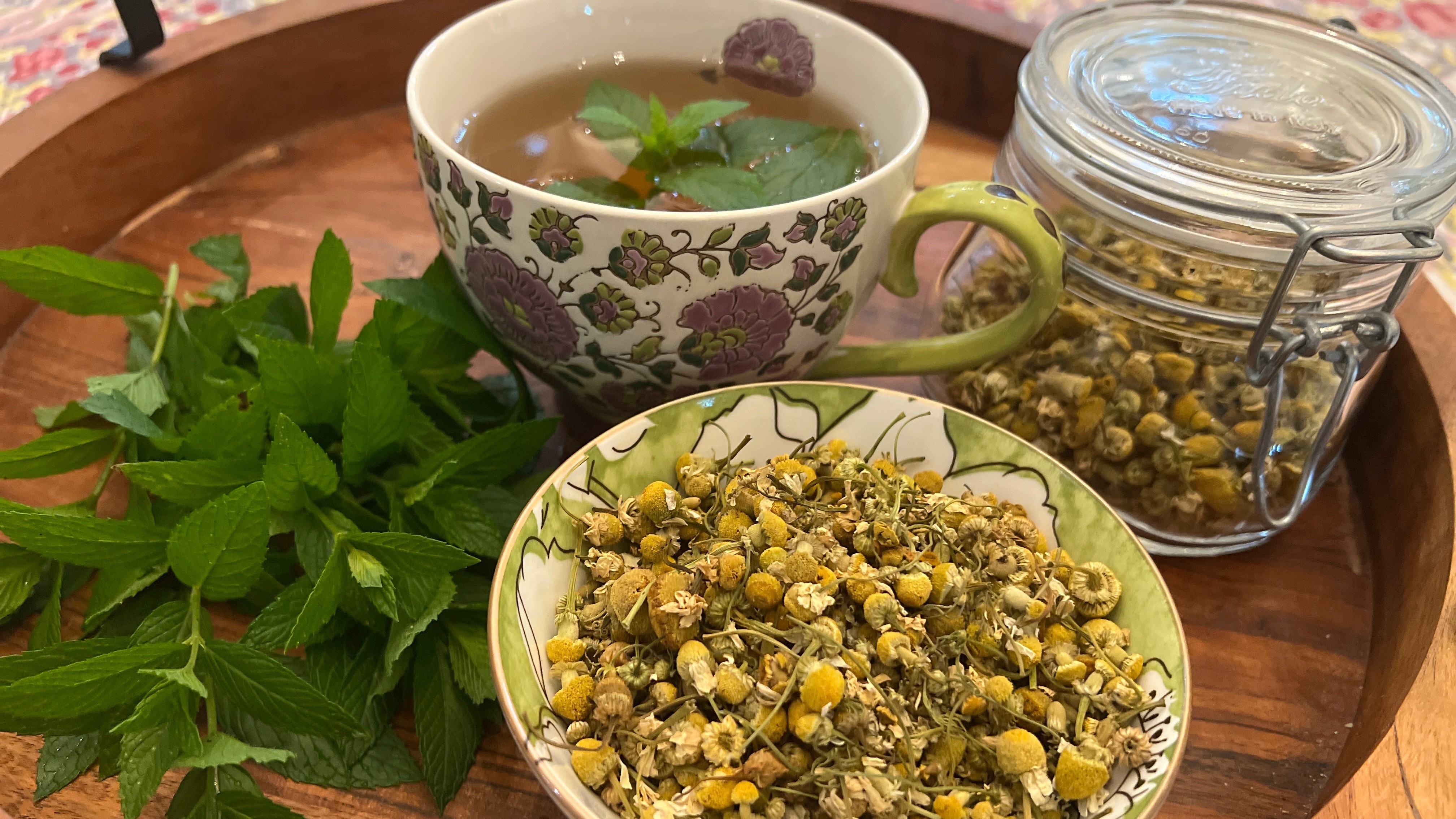 Freshly harvested spearmint leaves, dried chamomile flowers, and a cup of herbal tea.