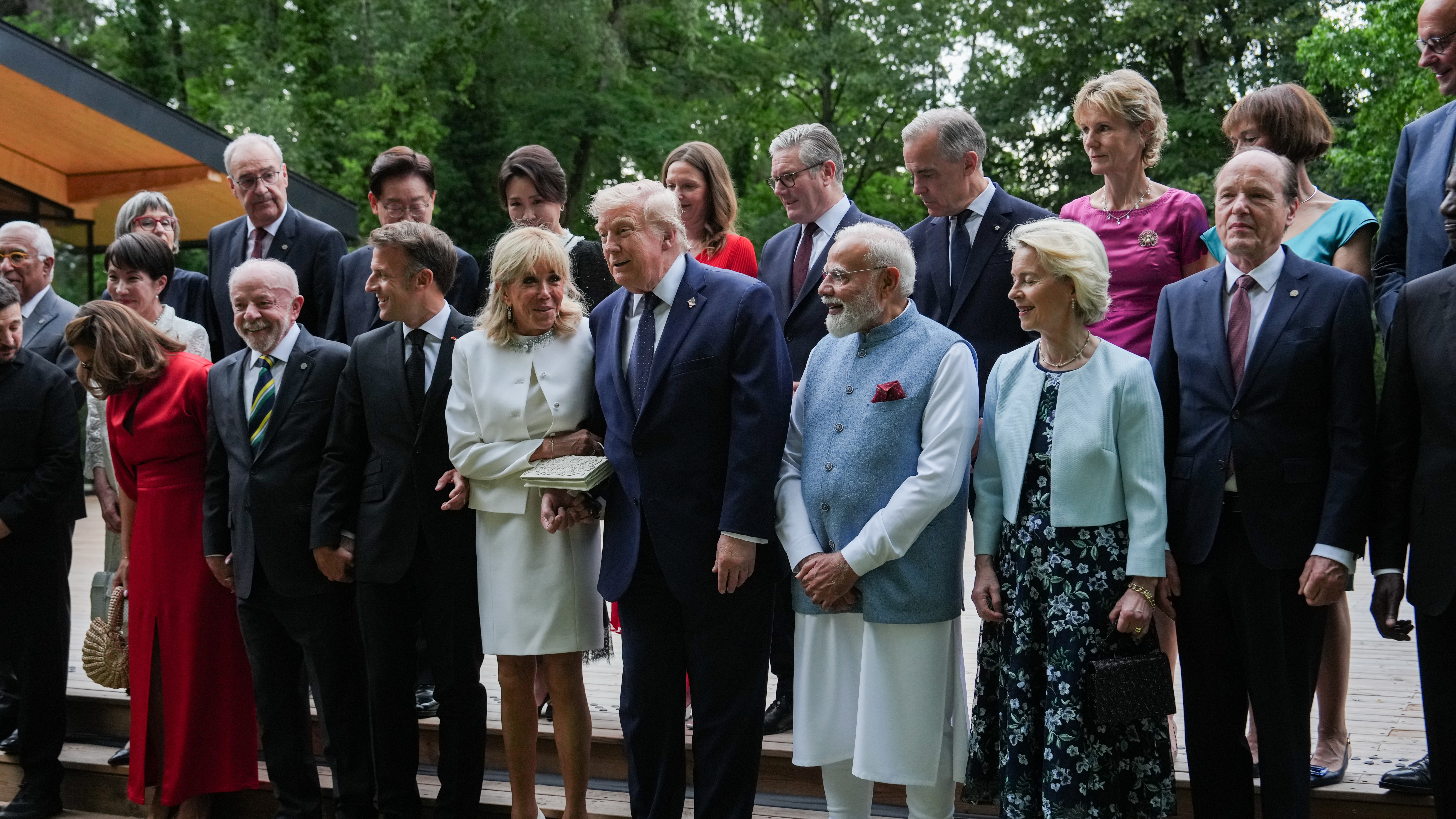 President Donald Trump helps France's first lady Brigitte Macron up a step as she arrives for a group photo with leaders and their spouses at the G7 summit.