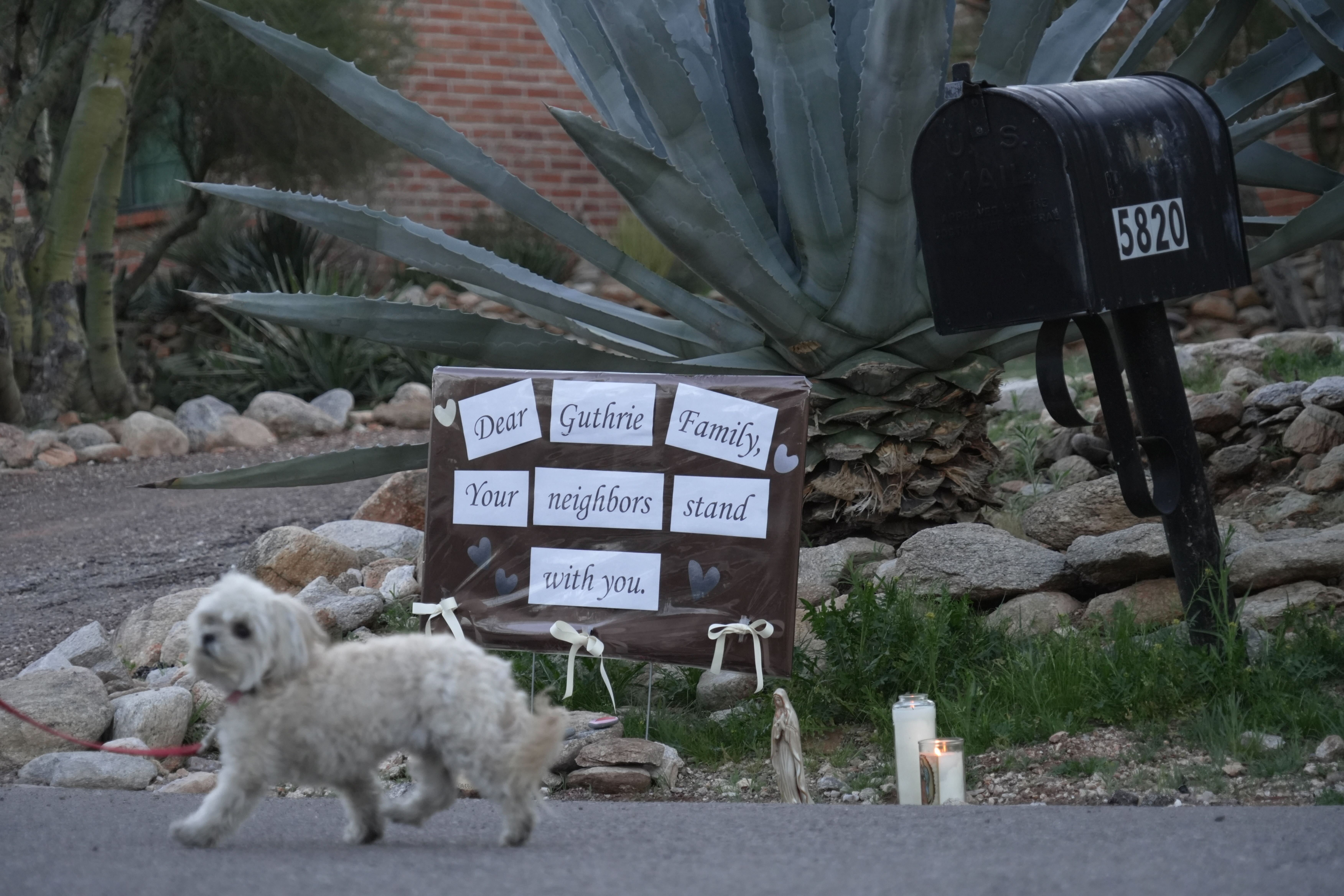 Lit candles next to a sign from neighbors supporting the Guthrie family outside of Nancy Guthrie’s house.
