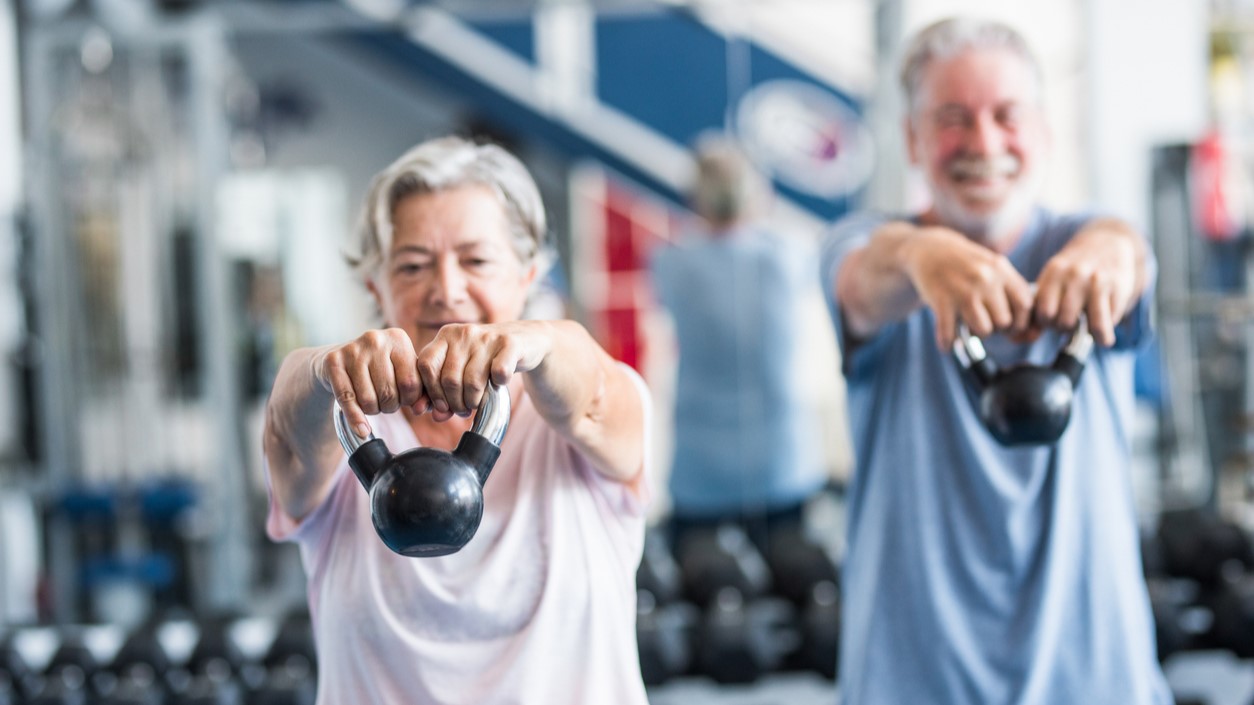 Two elderly people lifting weights together. 